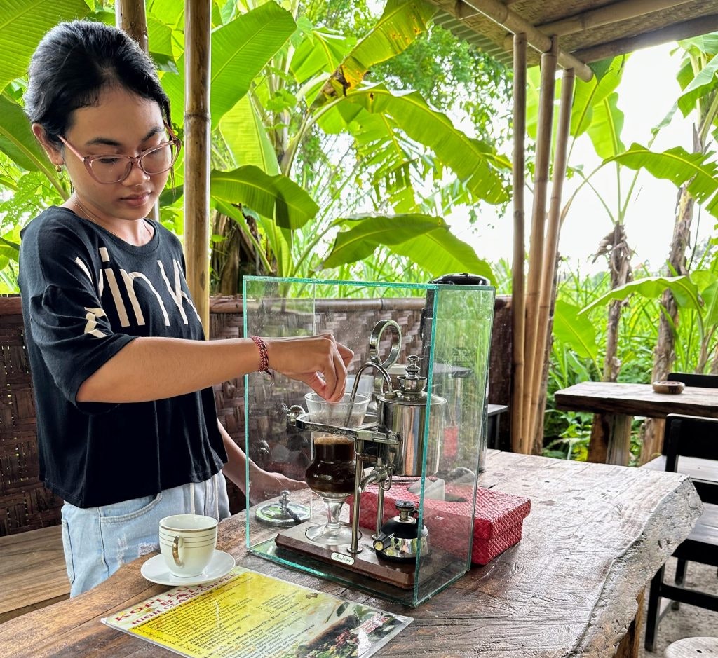 A woman preparing a cup of Kopi Luwak at a coffee farm in Bali, using traditional brewing methods.