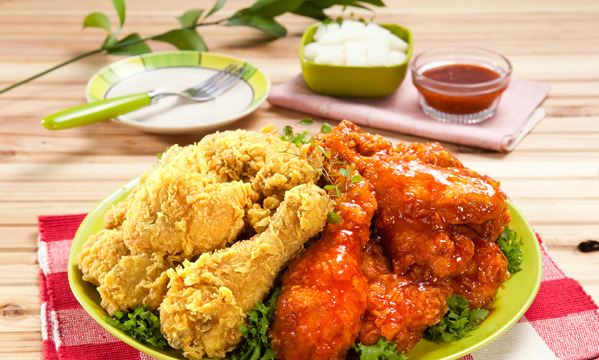 Plated Korean fried chicken with a spicy glazed portion, dipping sauce, and pickled radish on the side