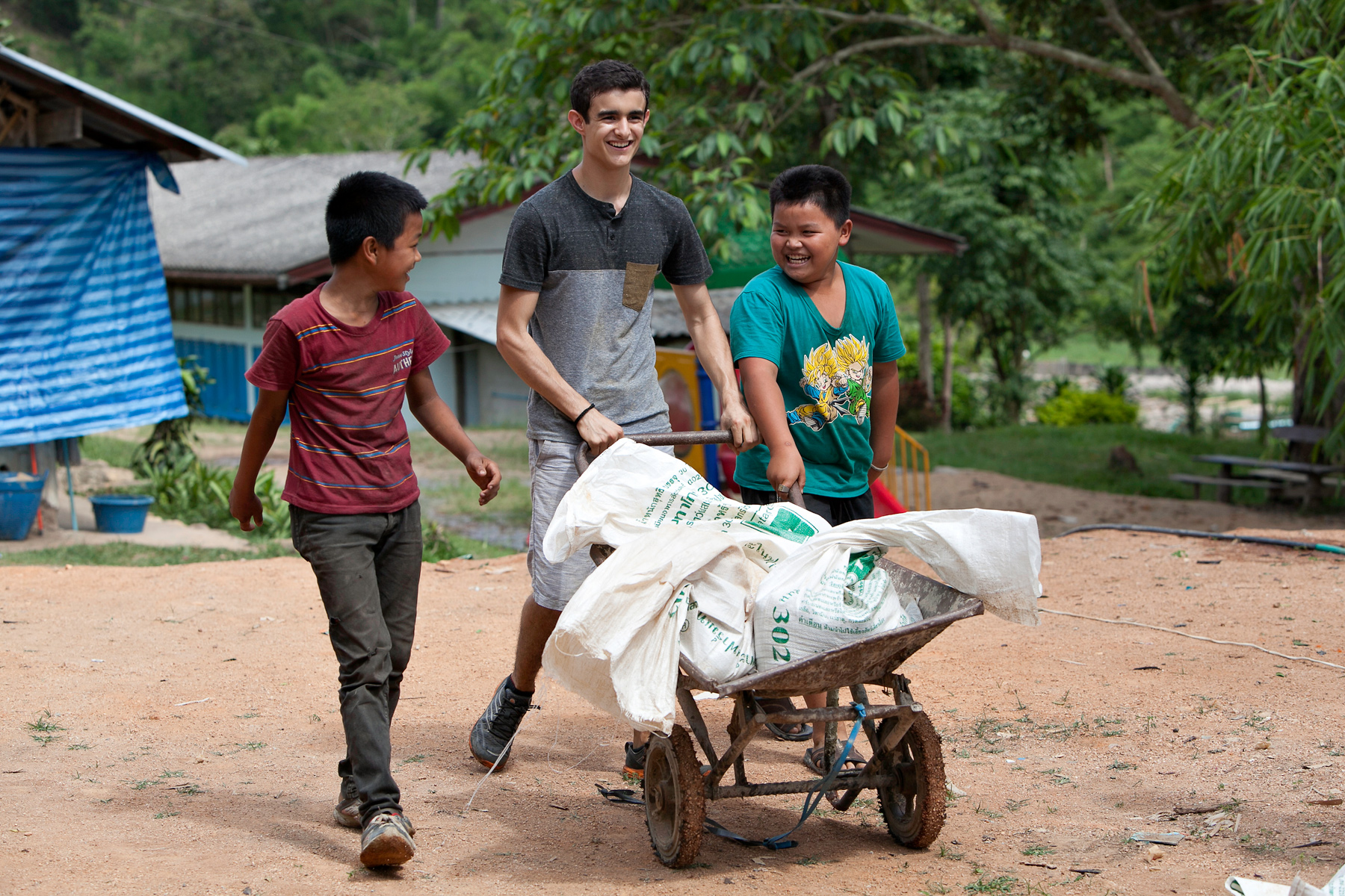 A student pushes a loaded wheelbarrow with local children on a village path