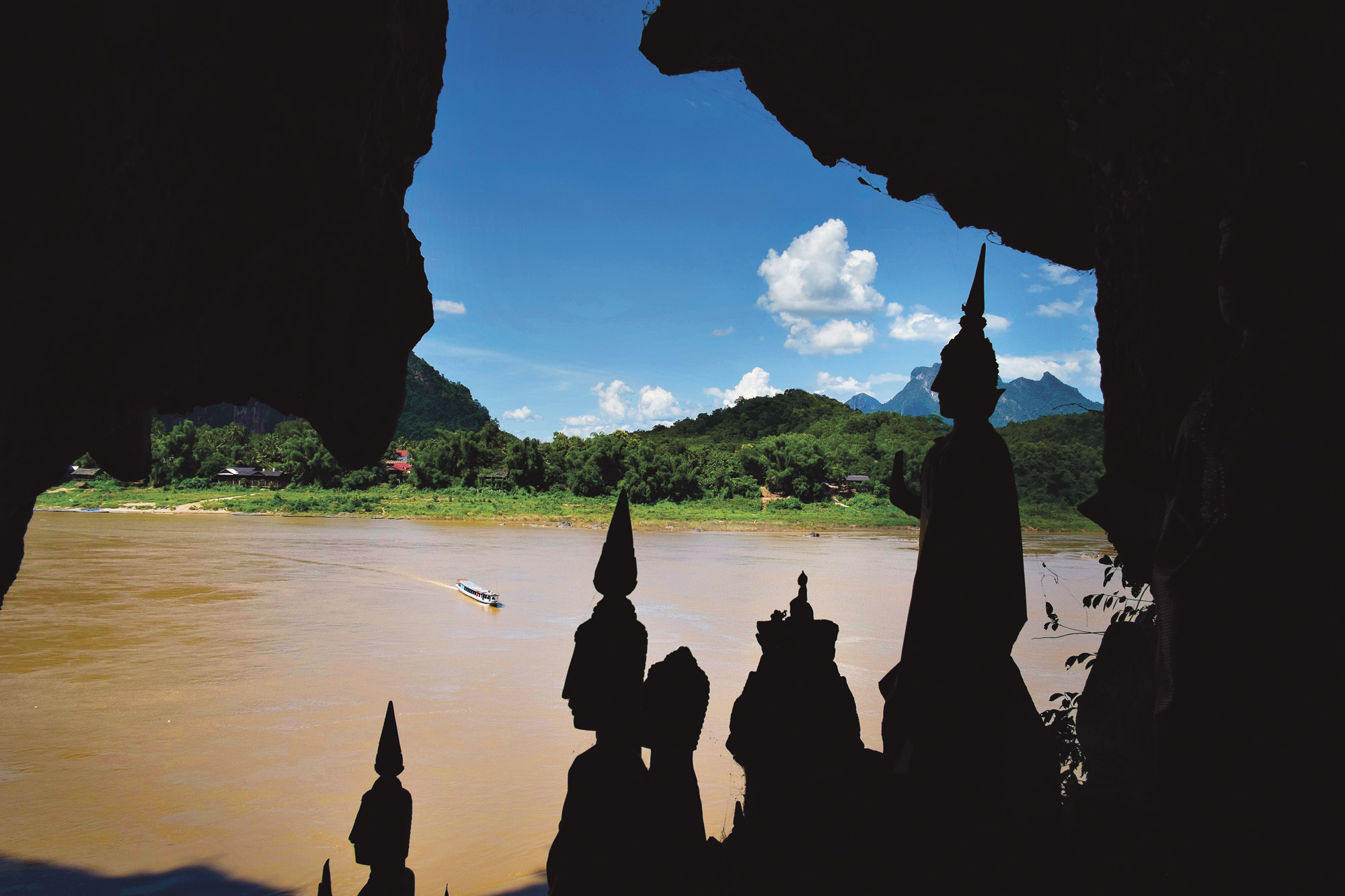 Silhouetted Buddha statues frame a view of the Mekong River from inside a cave
