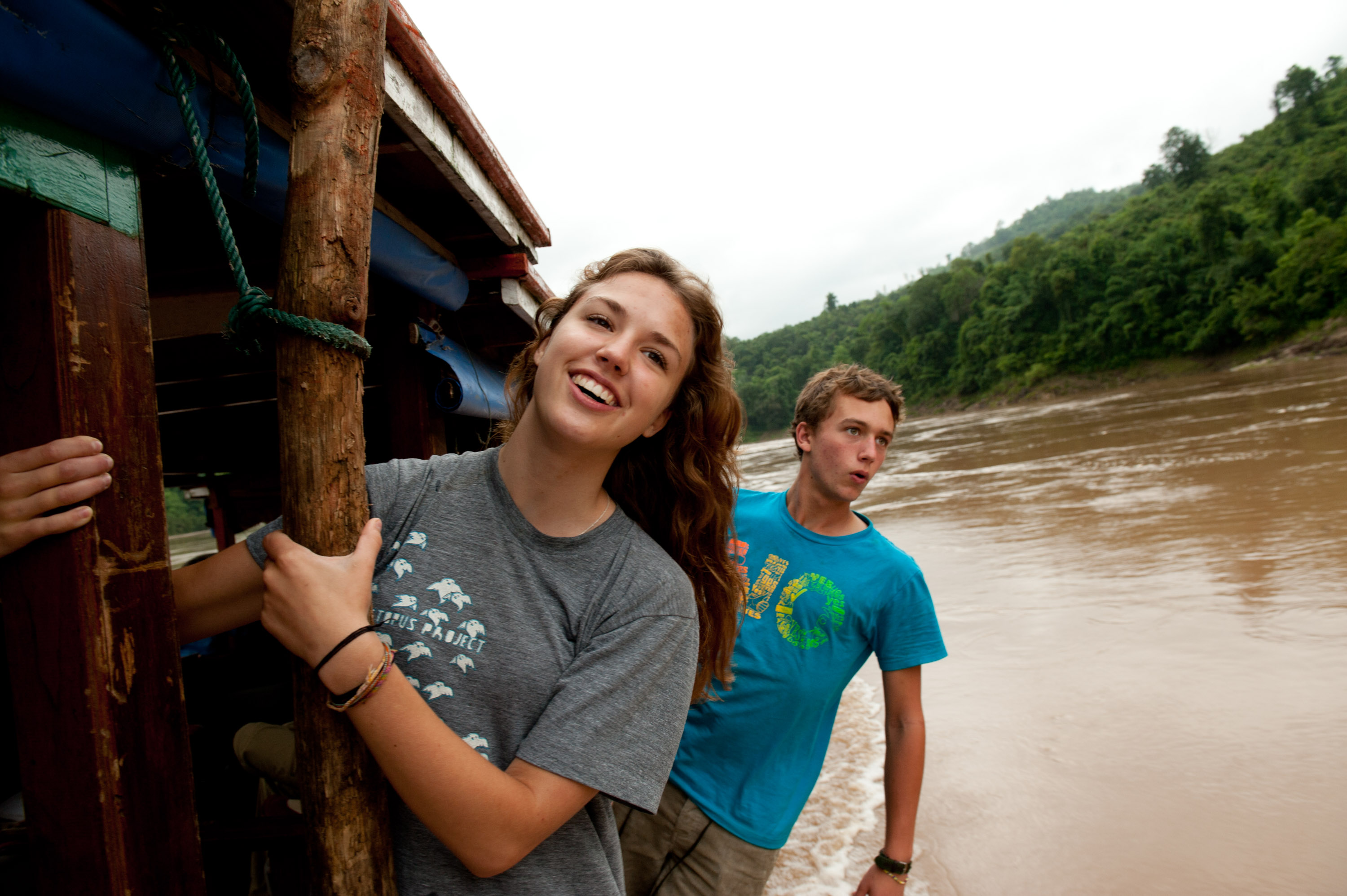 Students smile aboard a wooden boat on the muddy Mekong River