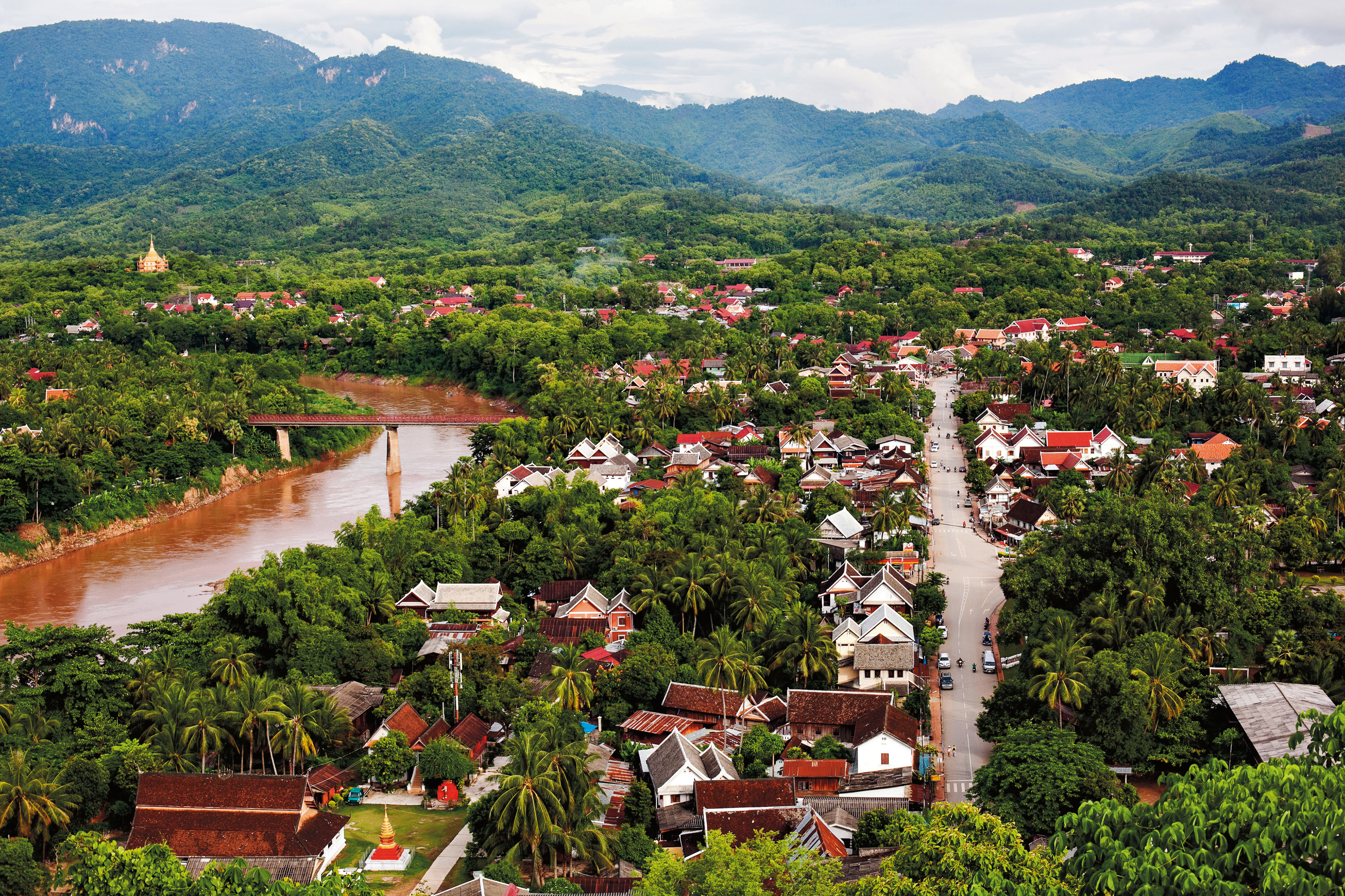 An elevated view over a wide river bend, with a riverside town and forested hills spreading to the horizon.