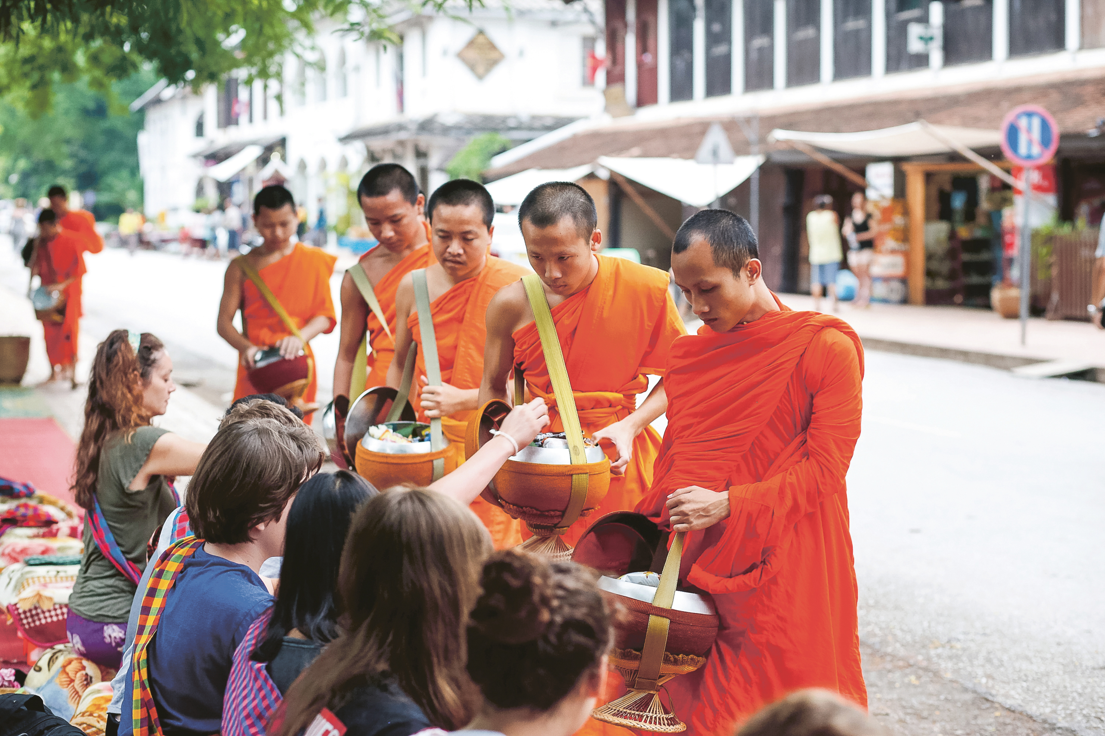 Saffron-robed monks walk a quiet street at dawn on a morning alms round.