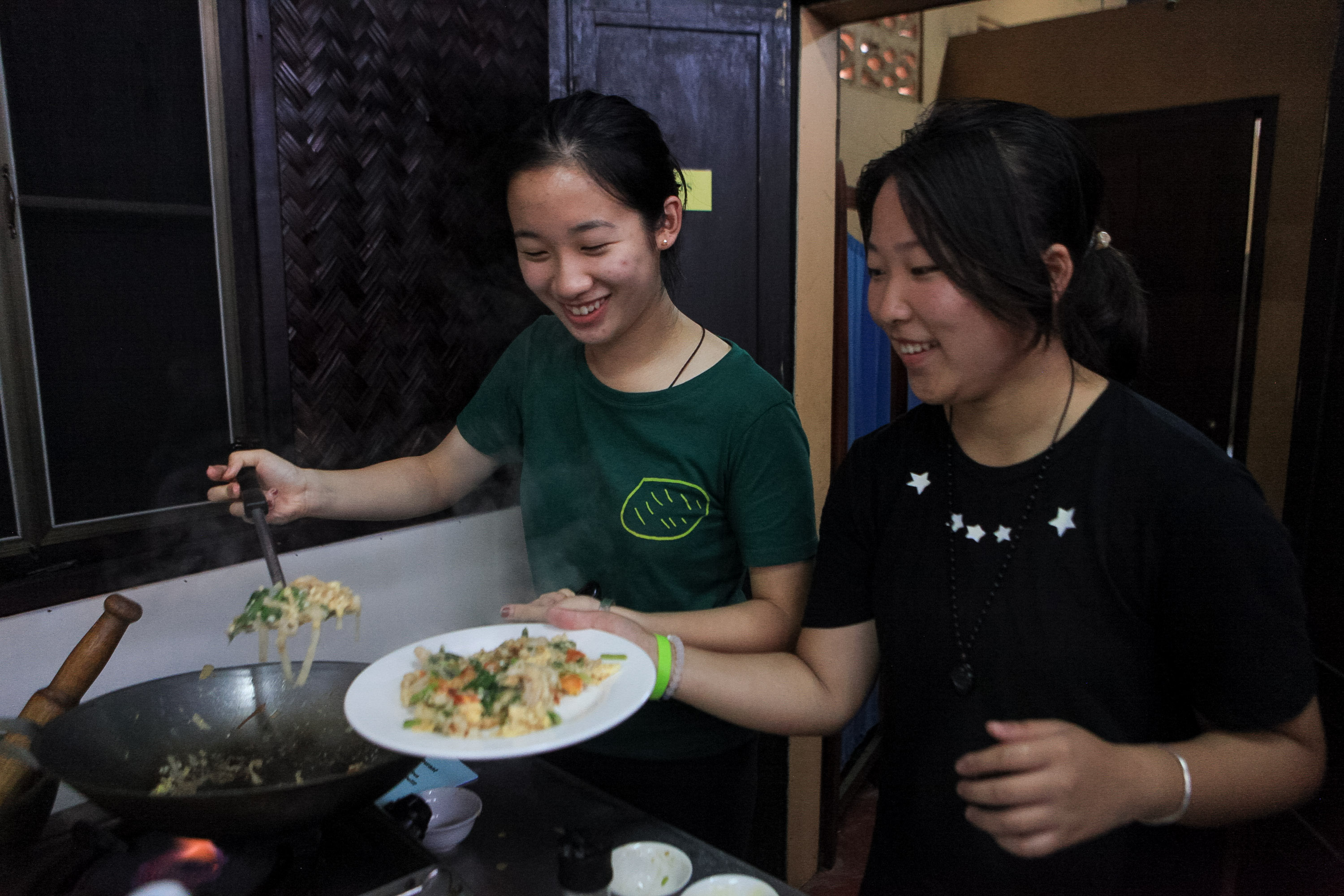 Two students cook a stir-fry dish together over a home kitchen stove.