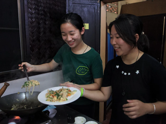 Two students cook a stir-fry dish together over a home kitchen stove.
