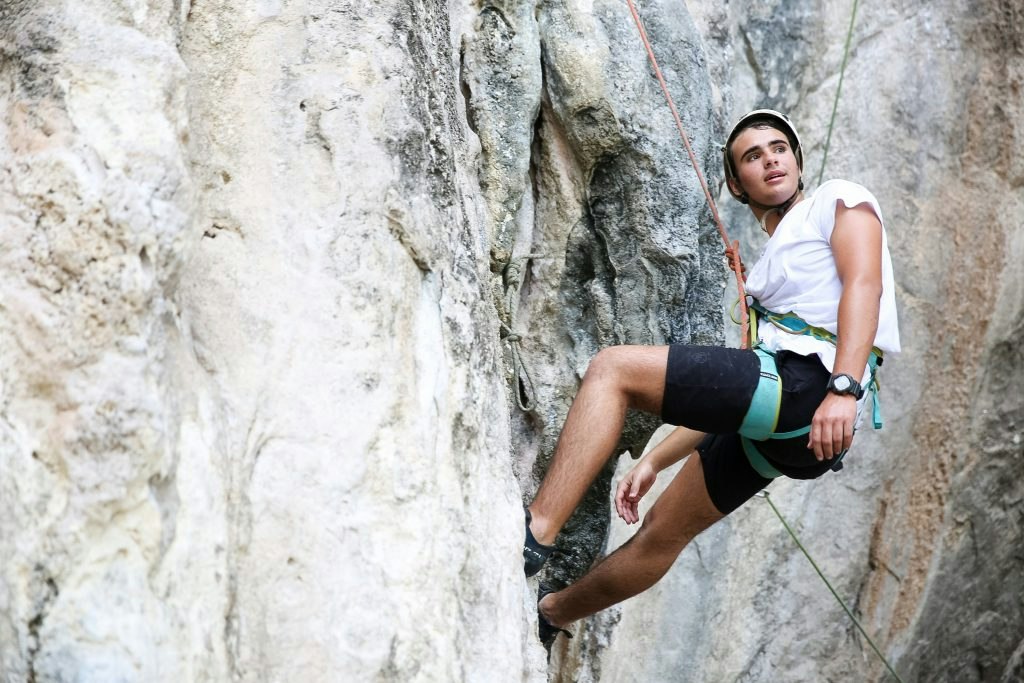 A teen traveler in a helmet and harness rock climbs a limestone cliff during an adventure program in Thailand.