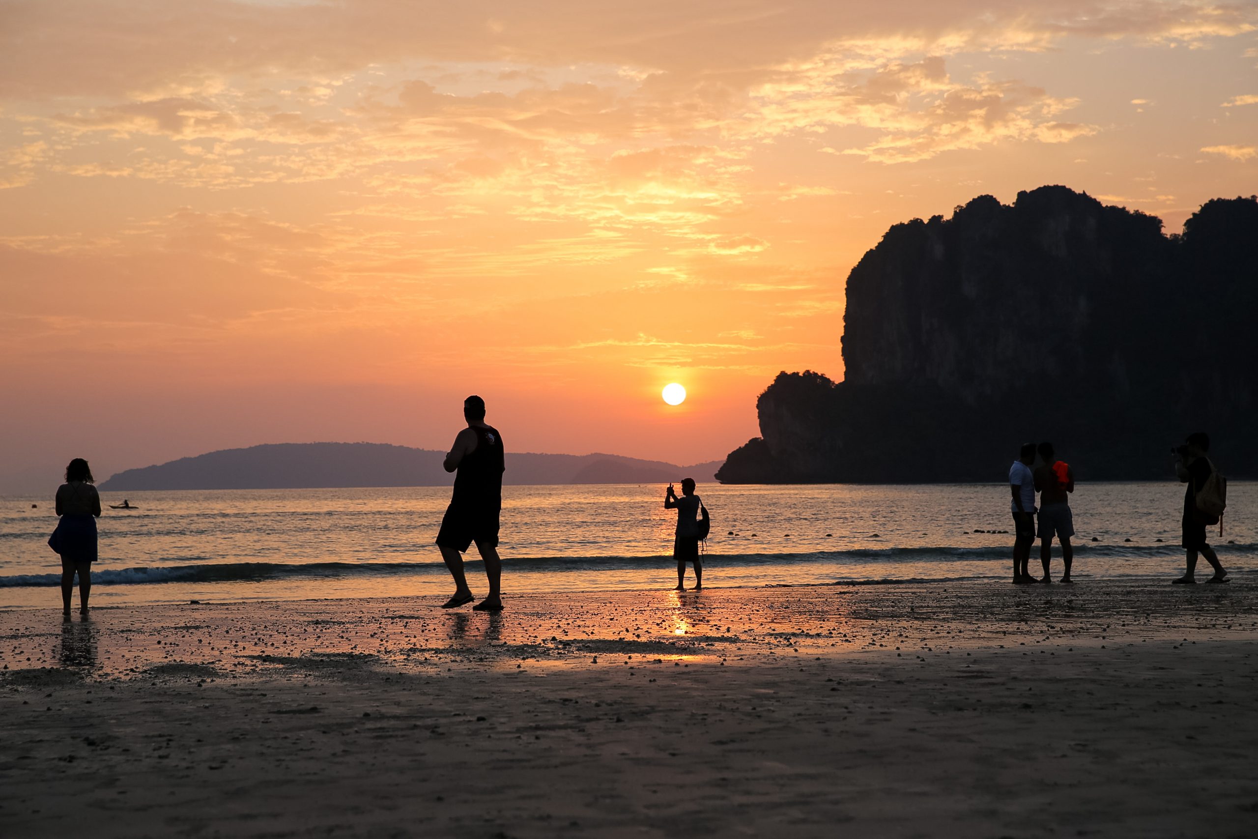 Students silhouetted on a beach at sunset with limestone cliffs in the distance