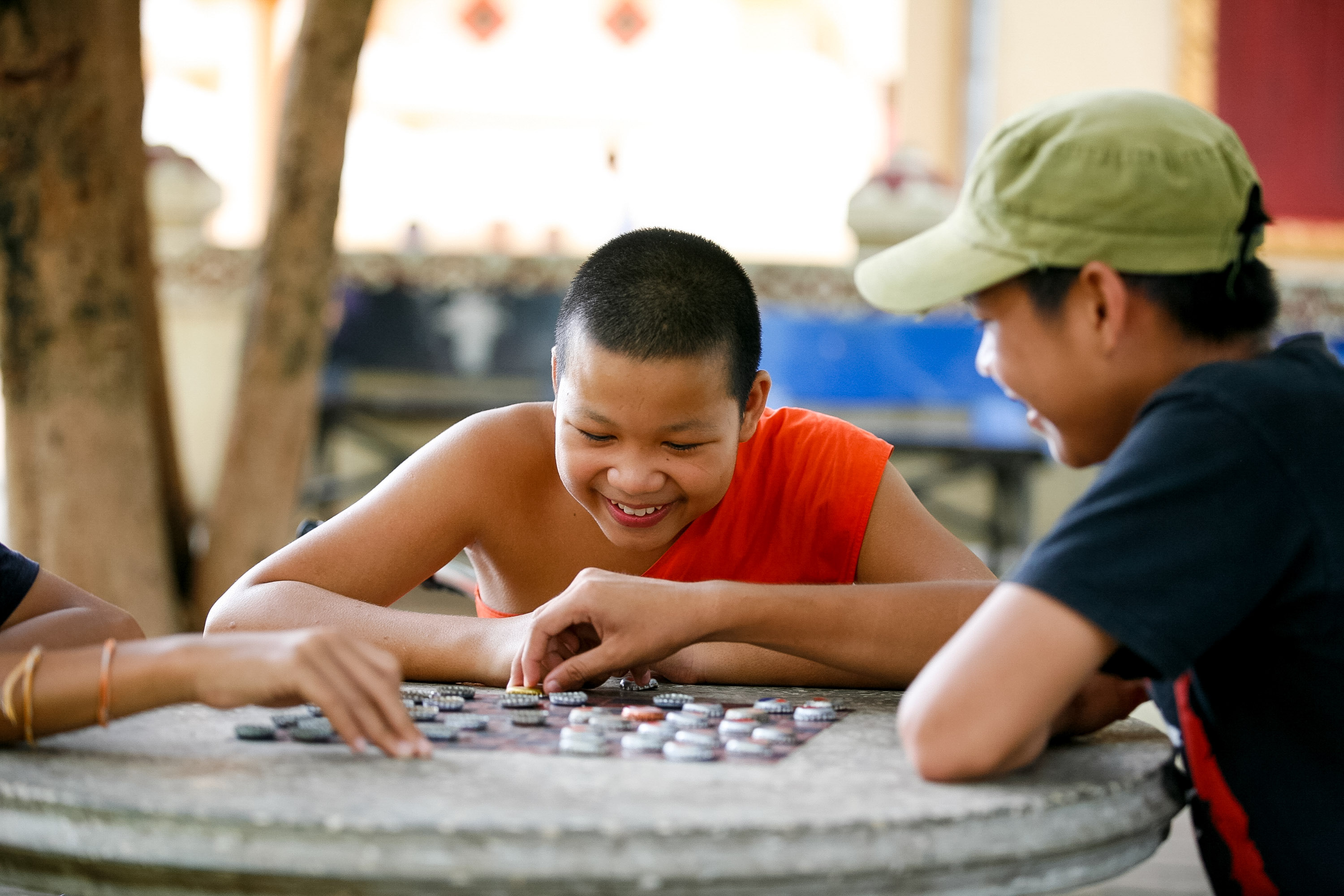 A young monk plays a board game with a friend at an outdoor stone table