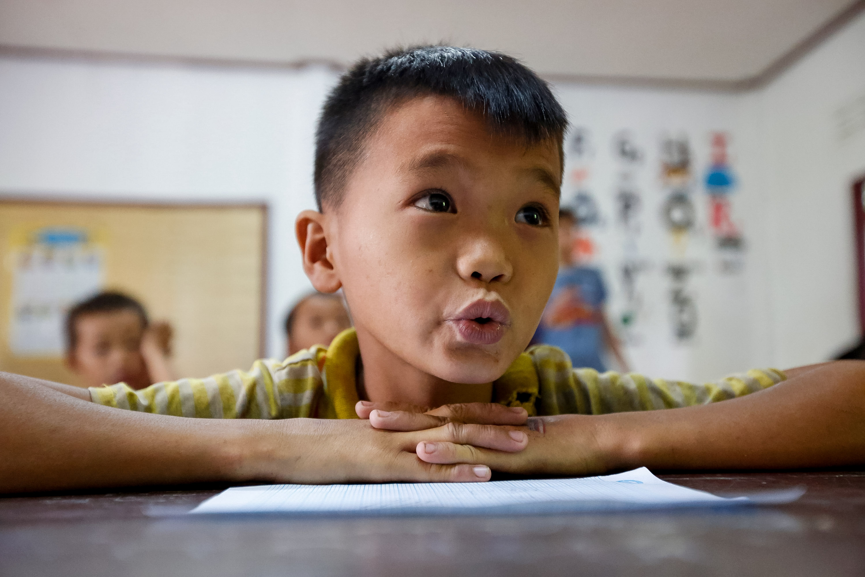 A young student rests on folded arms at a classroom desk