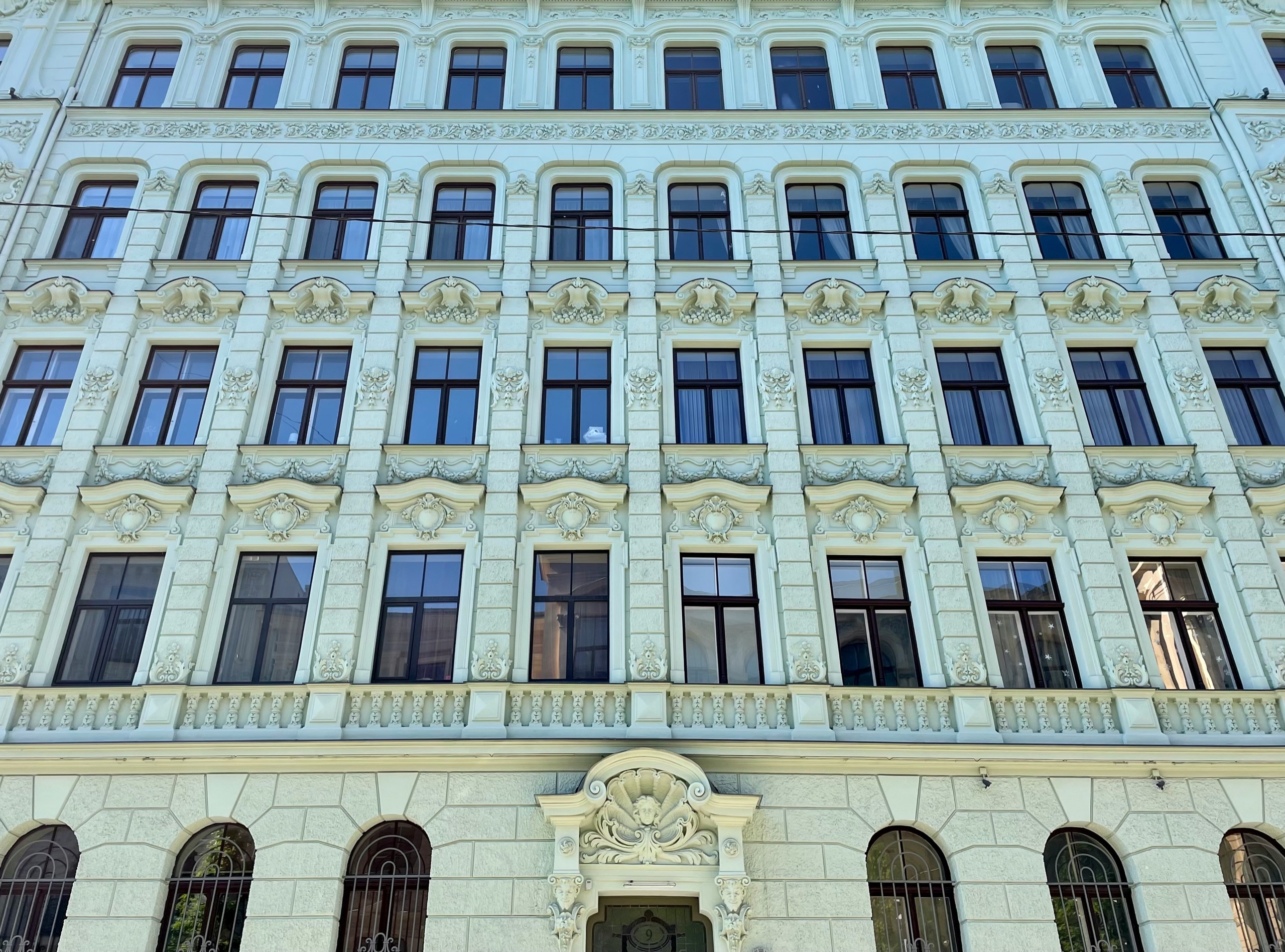 A pale blue Art Nouveau facade rises in rows of tall windows, with carved ornament over the arched doorway.