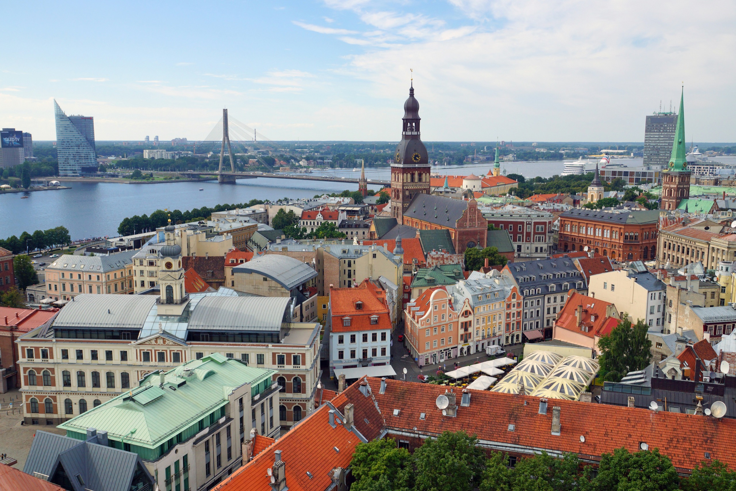 Red-tiled roofs and a cathedral spire crowd an old town beside a wide river and a cable-stayed bridge, under an open sky.