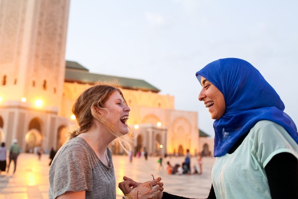 A student traveler and a local woman laughing while talking together in front of a mosque in Morocco.