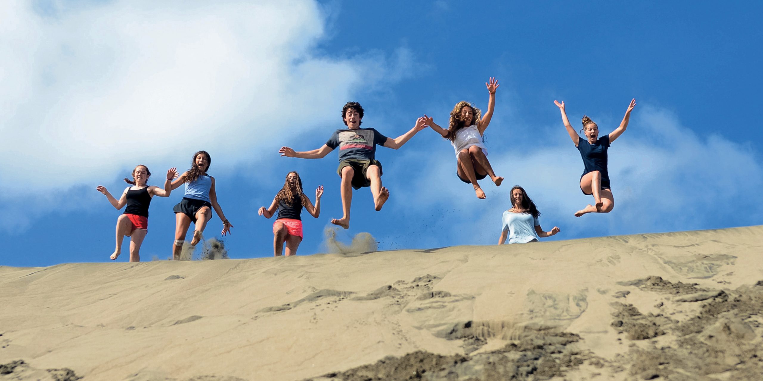 Life skills for teens: teen travelers jumping off a sand dune in Fiji during a transformational student travel program.