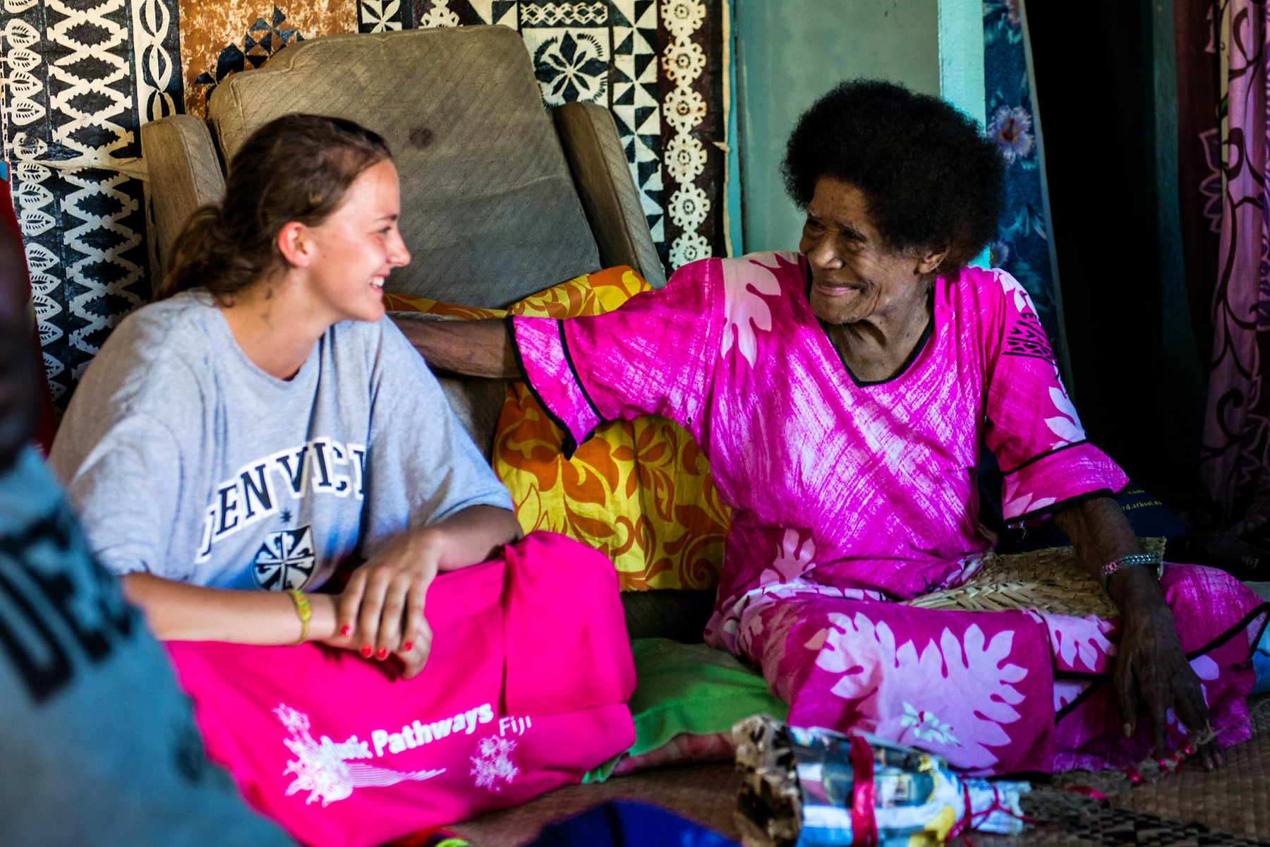 A student shares a laugh with a local Fijian woman inside a woven-walled home in Fiji