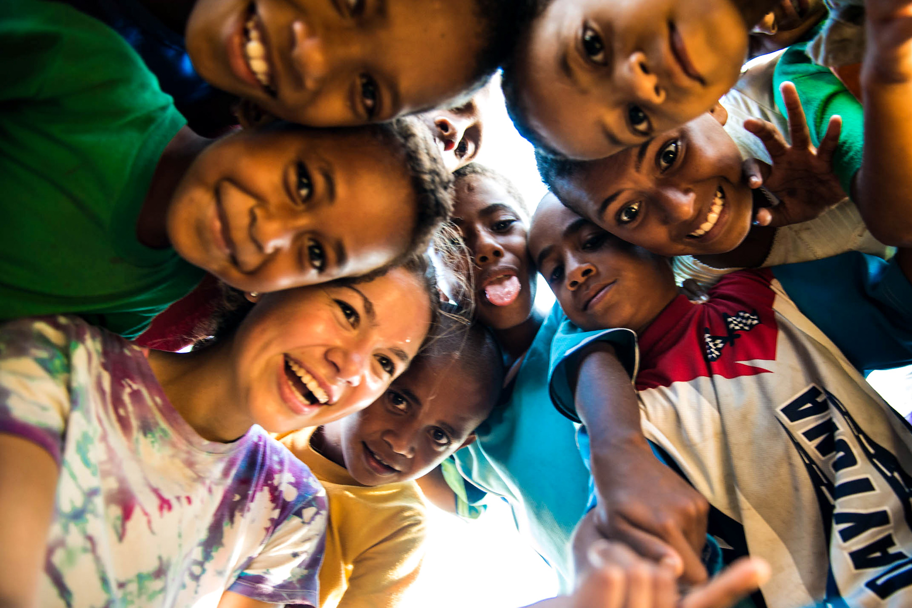 Local children and a student huddle close together, smiling up at the camera