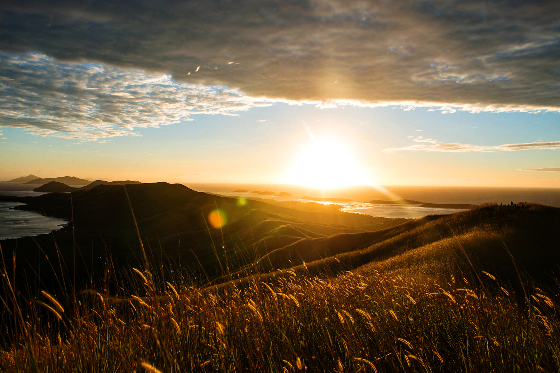 Sun sets over hills and coastline, with grass in the foreground