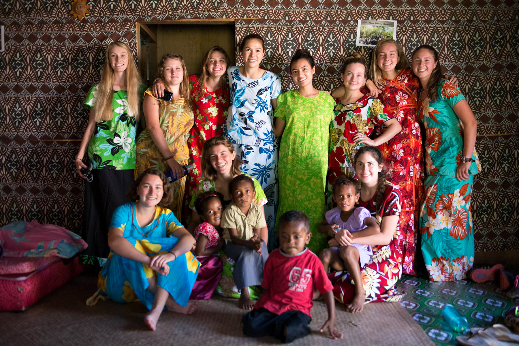 Students and local children pose together in colorful traditional dress inside a home