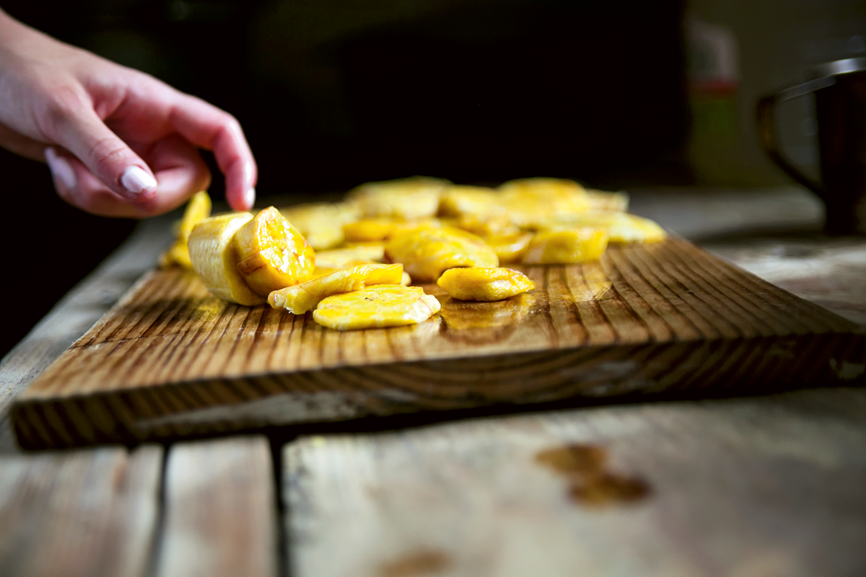 Teen travelers arrange pieces of fried plantain on a wooden cutting board