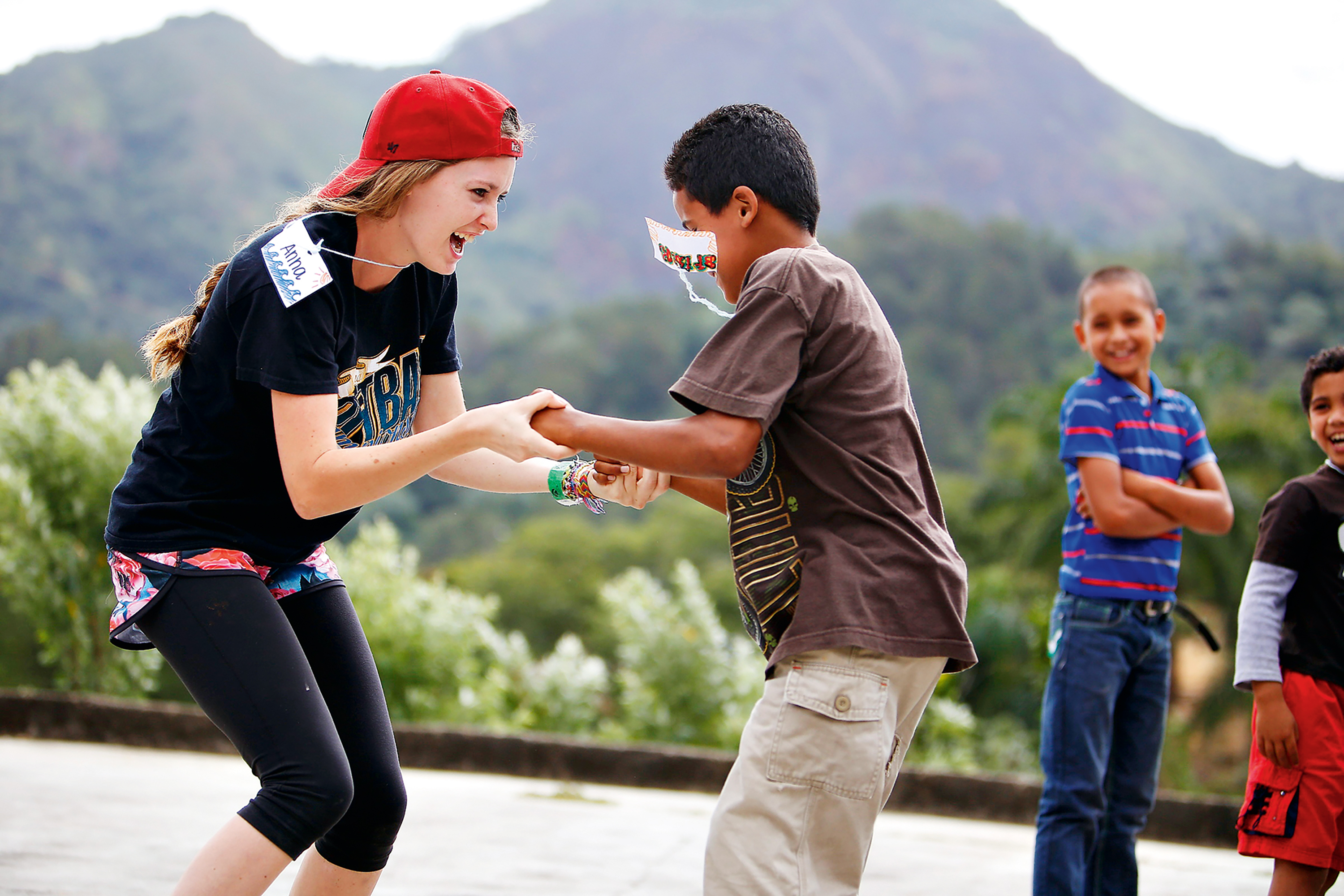 A student and a local child laugh while playing a hand-clapping game in Dominican Republic with mountains behind them