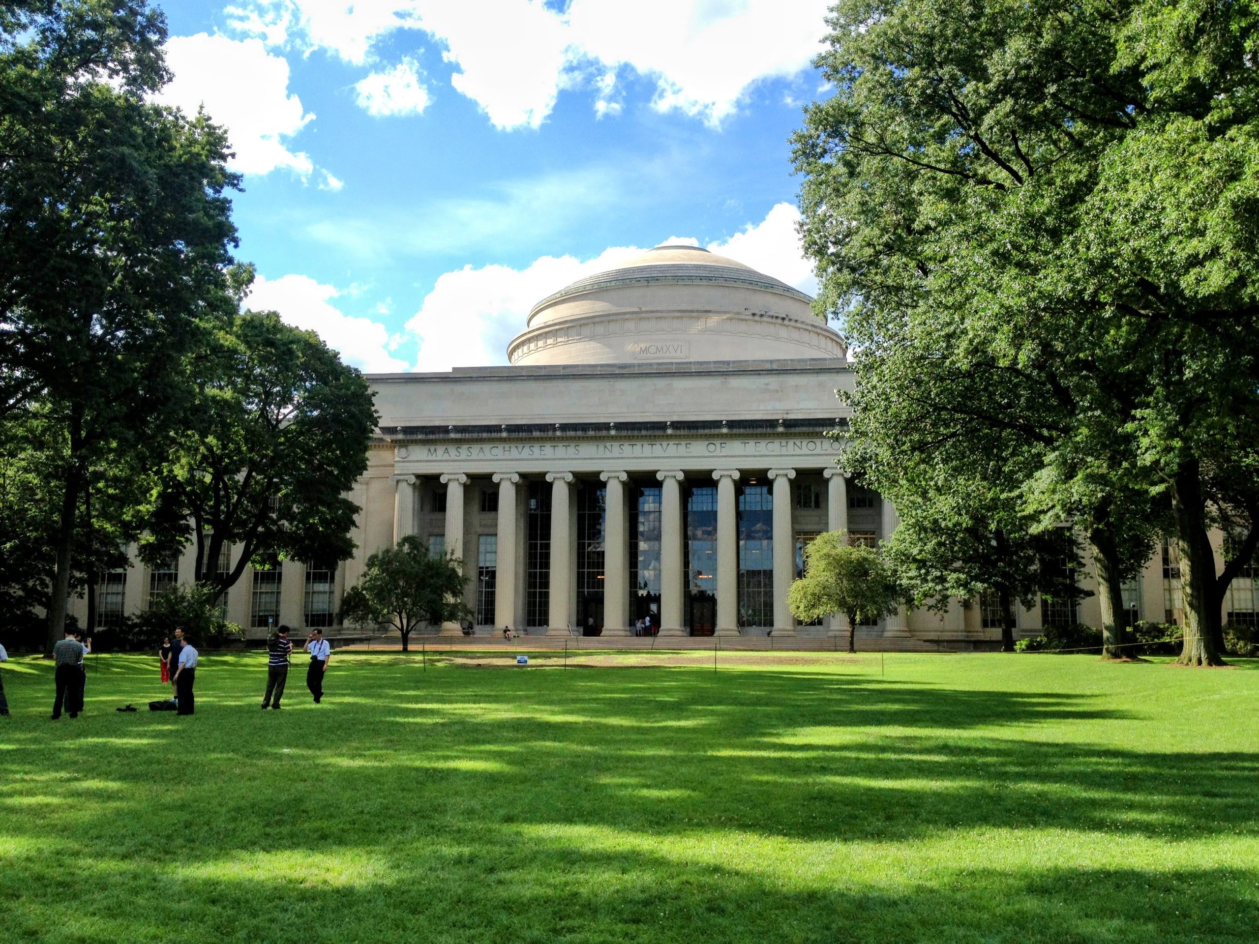 Students walk across a grassy lawn in front of a domed university building with a columned entrance