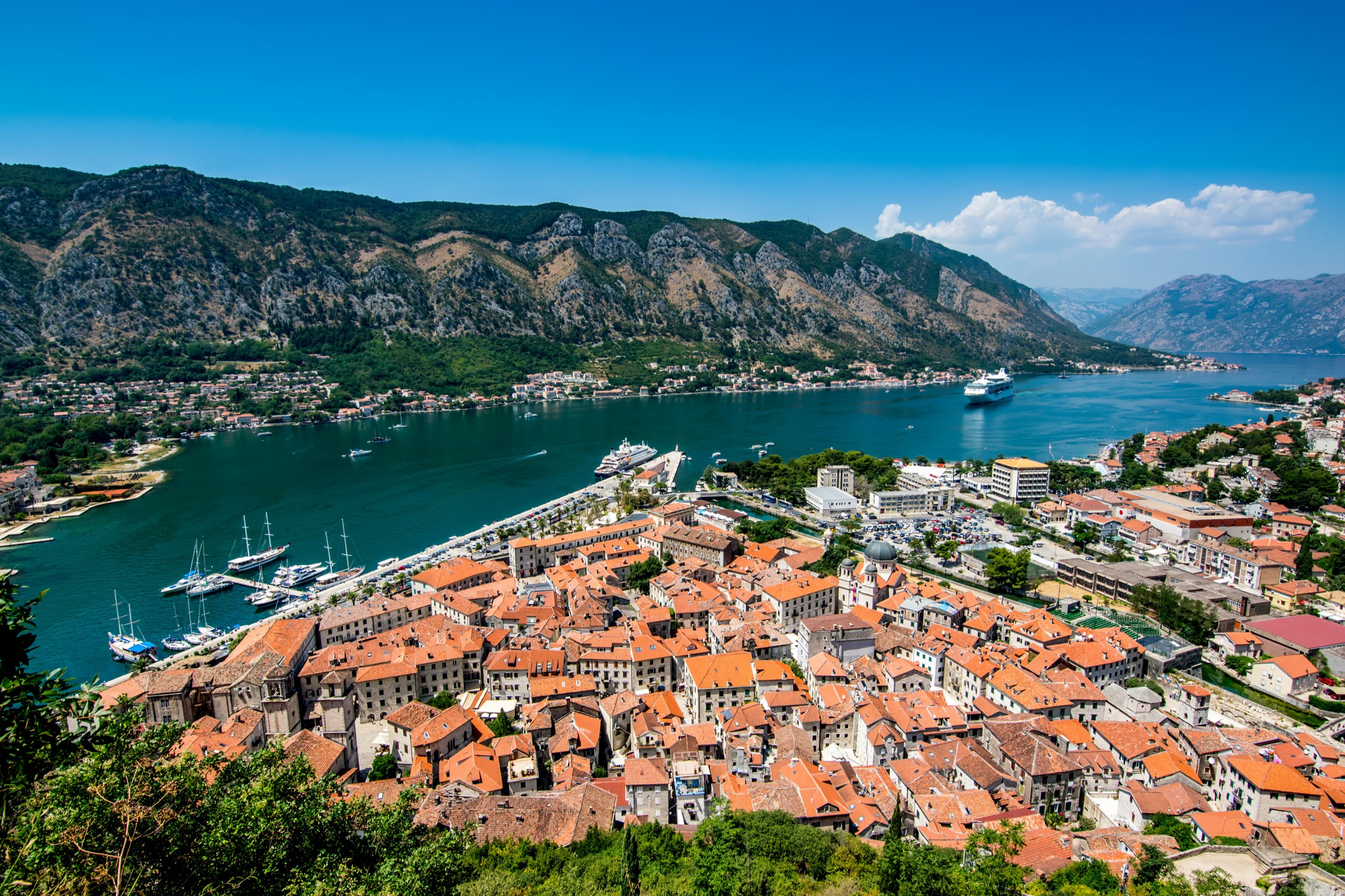 An aerial view of the walled town of Kotor at the foot of steep mountains where they meet the bay.