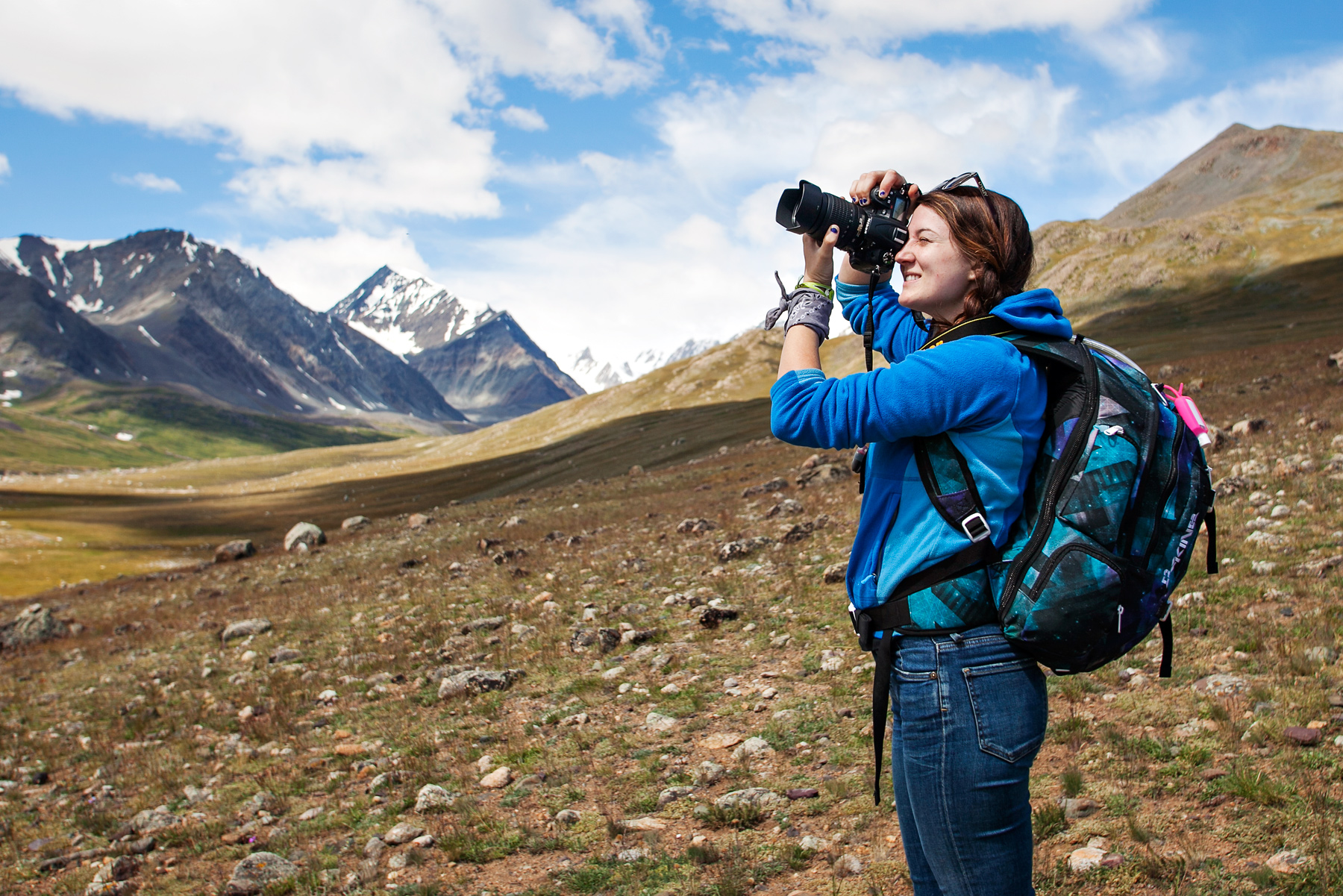 A student photographs snow-capped mountains across a grassy valley