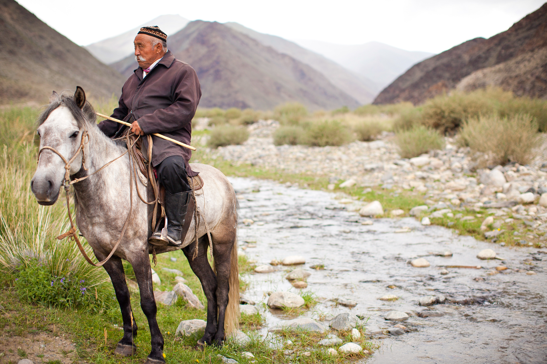 Students watch a local herder on horseback beside a rocky stream in the Mongolian mountains