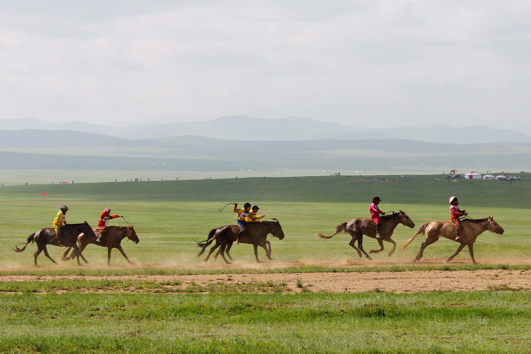 Riders race horses across the open Mongolian steppe