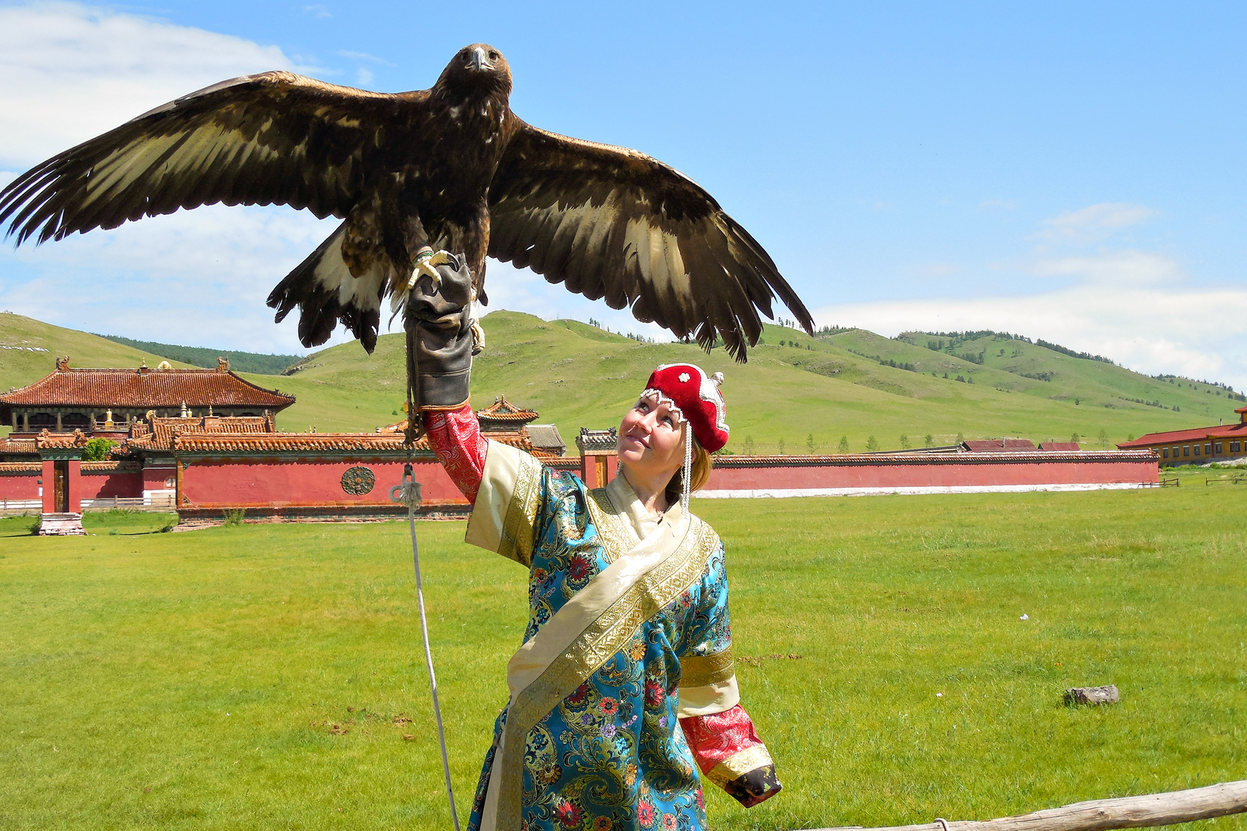 Teen travelers dress in traditional Mongolian attire and hold a golden eagle on the arm