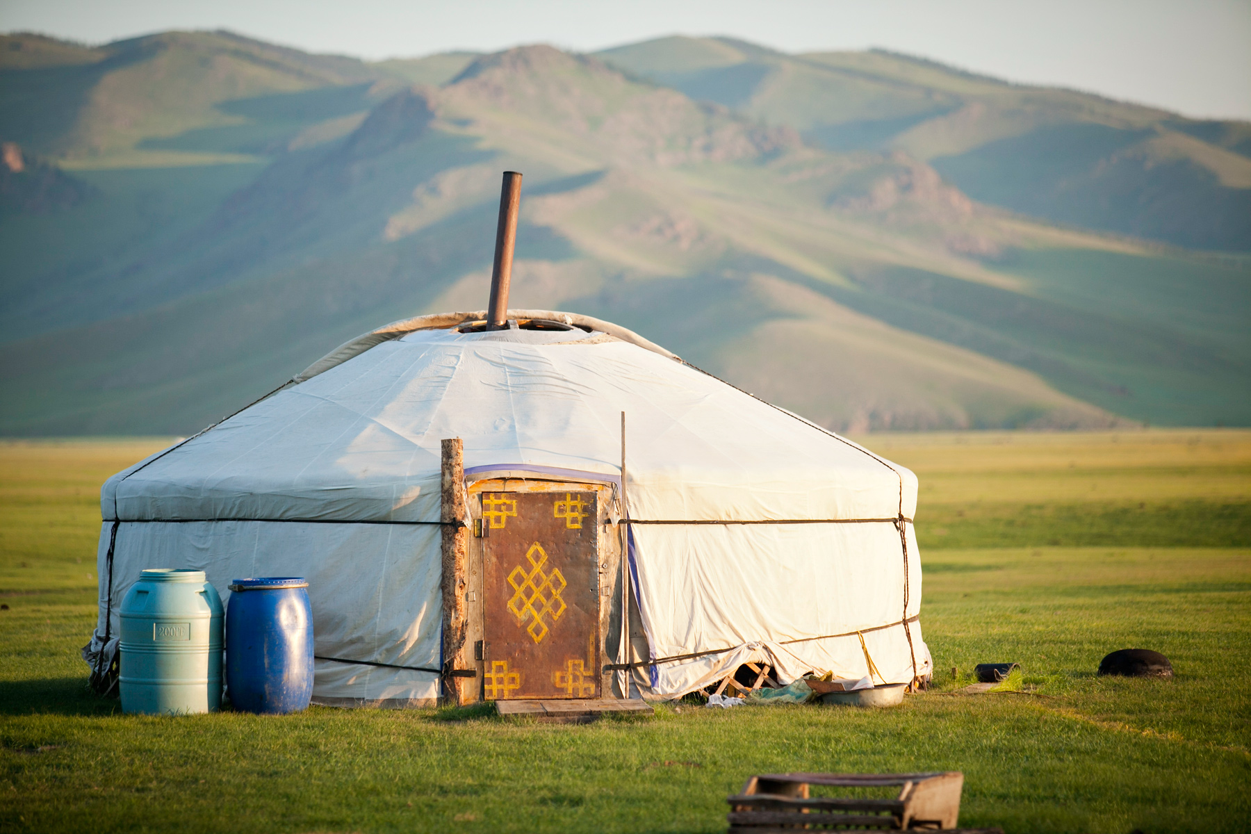 A traditional white ger stands in a grassy valley with mountains behind it