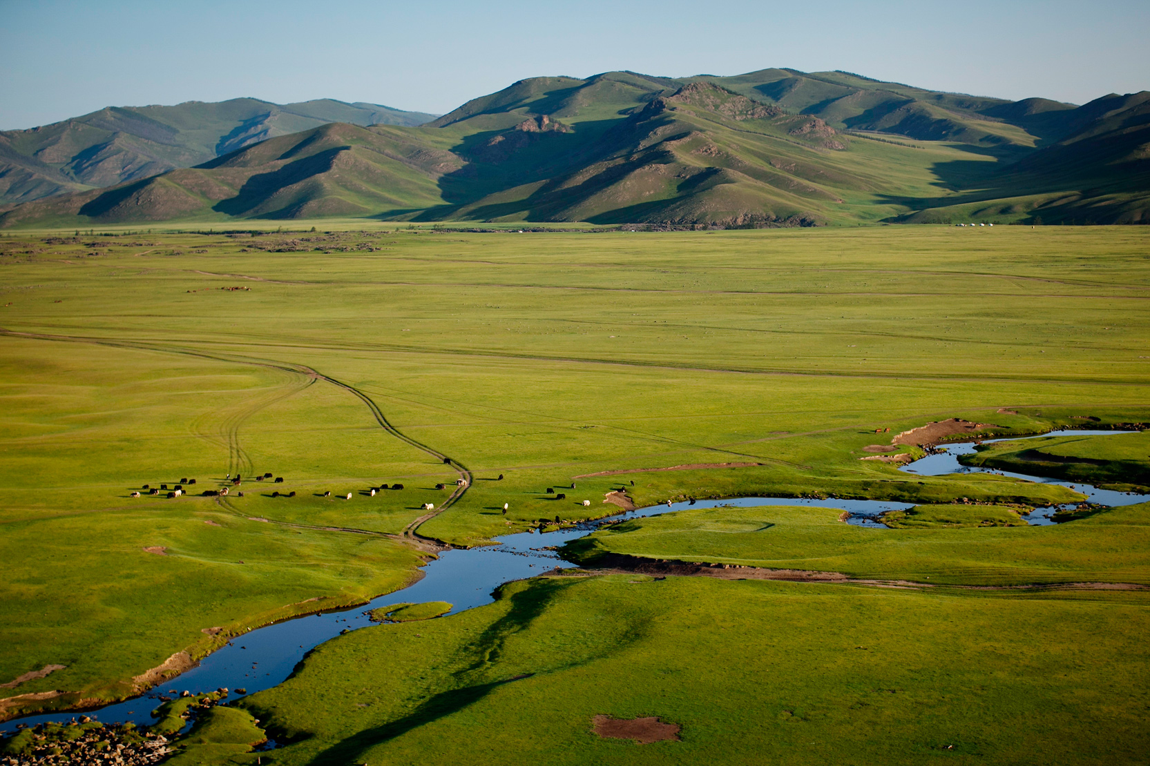 A winding river cuts through a wide green Mongolian steppe valley below mountains