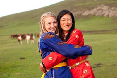During a teen tour in Asia, a student and a Mongolian woman wearing traditional clothing smile and embrace.