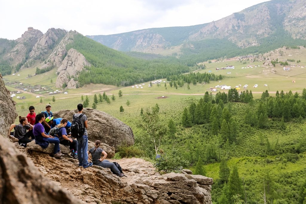 Group of teens resting on a rock with the vast landscape of Bayan-Ulgii, Mongolia in the background.