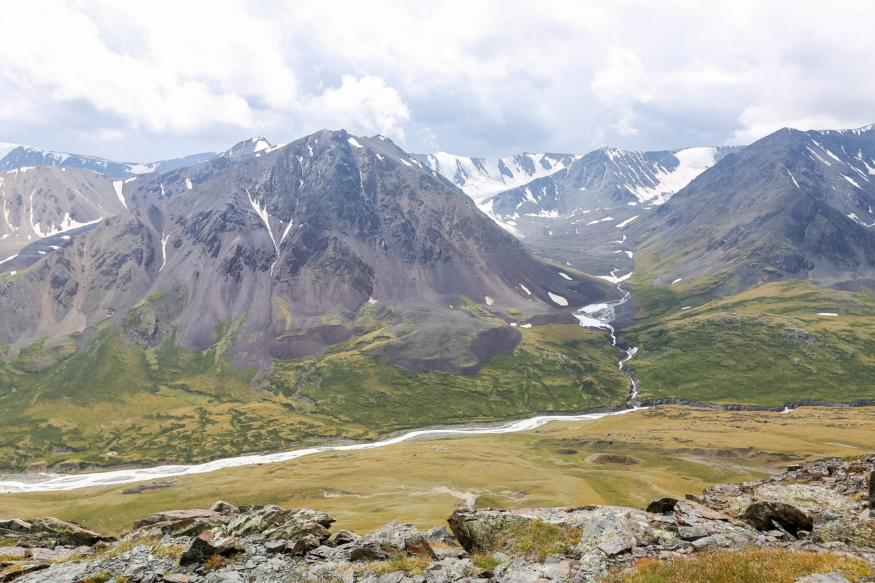 Snow-streaked mountains rise above a green valley with a winding river