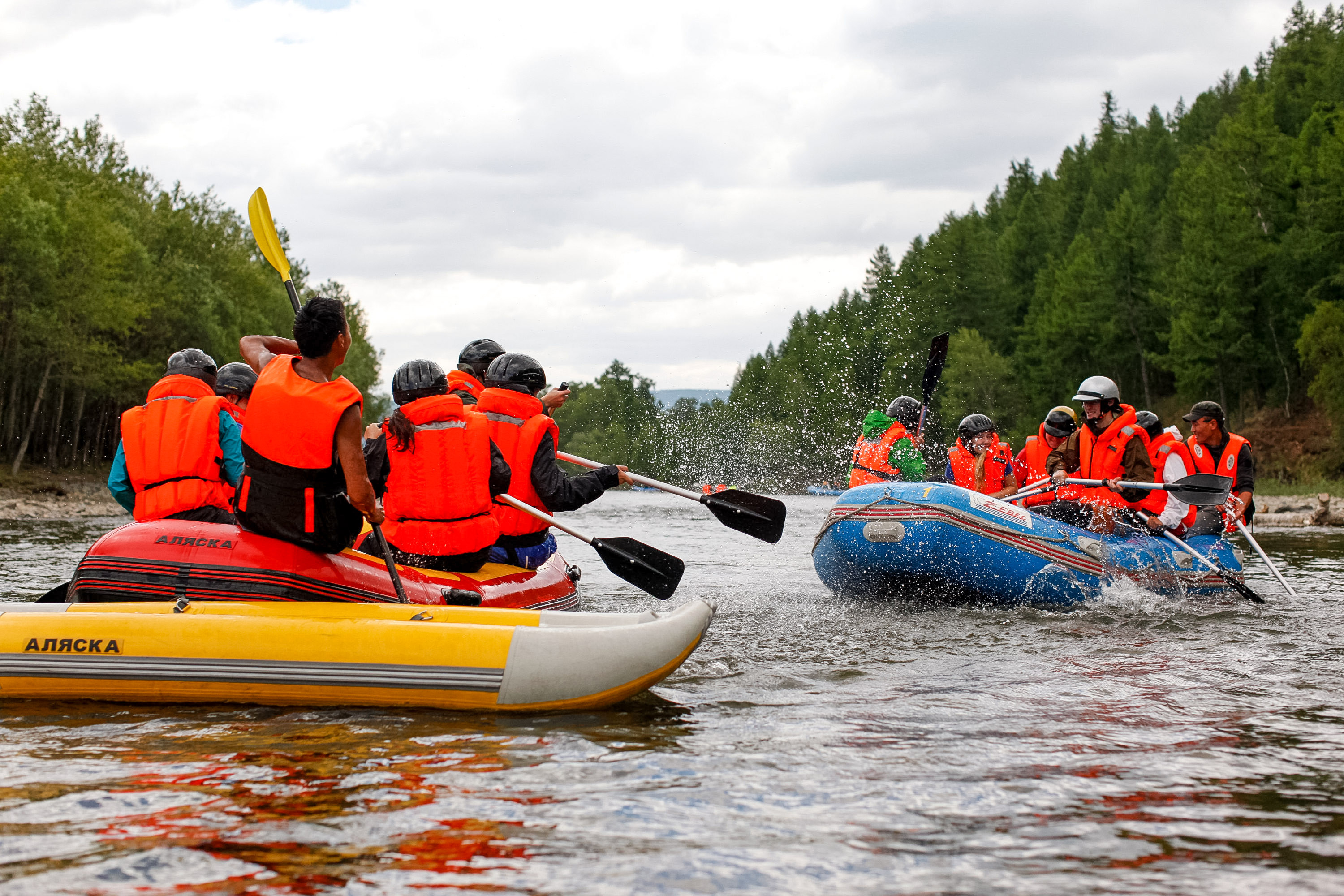 A school trip in life jackets paddles inflatable rafts through splashing river water