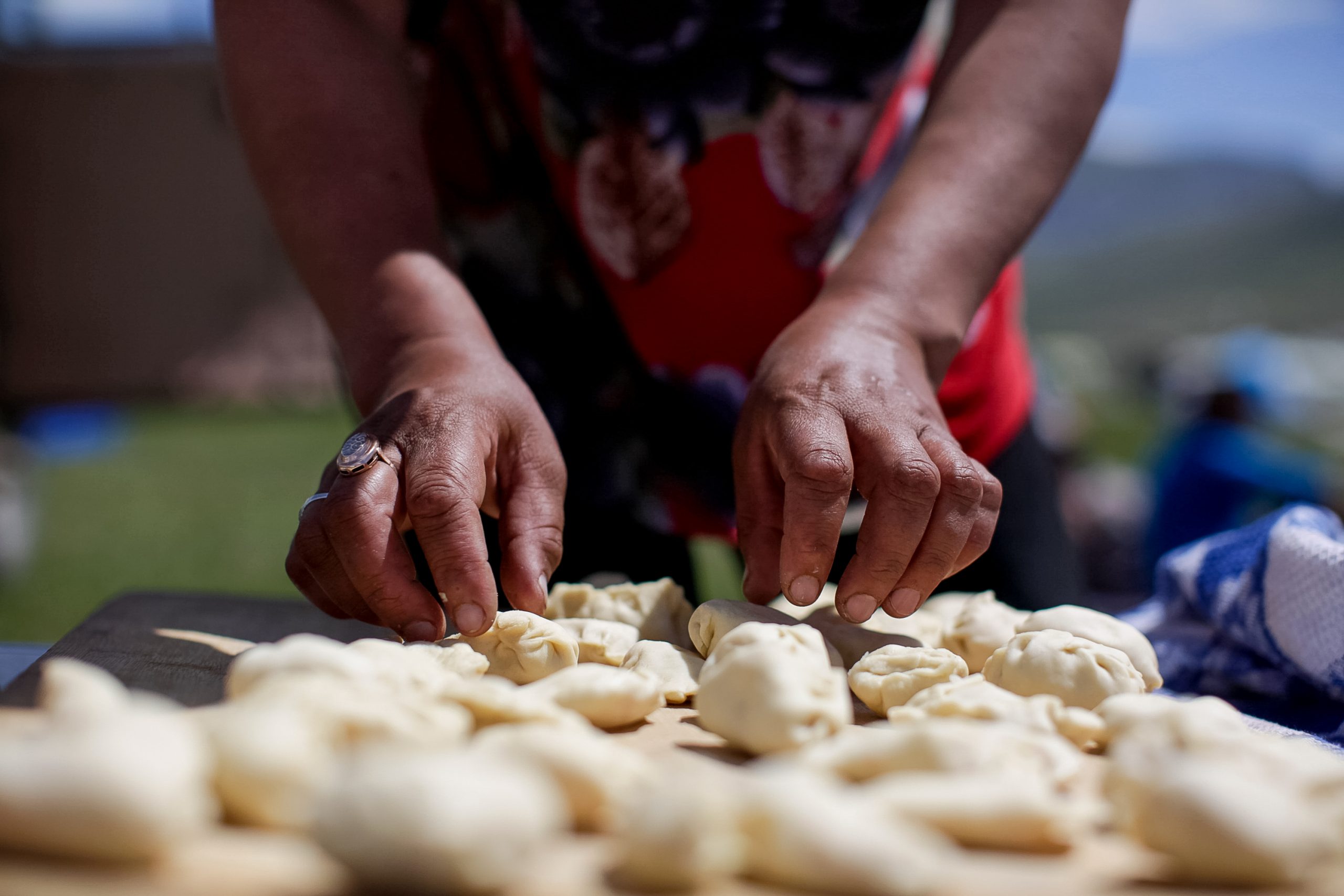 A pair of hands pinches rows of small dough dumplings closed on a wooden board.