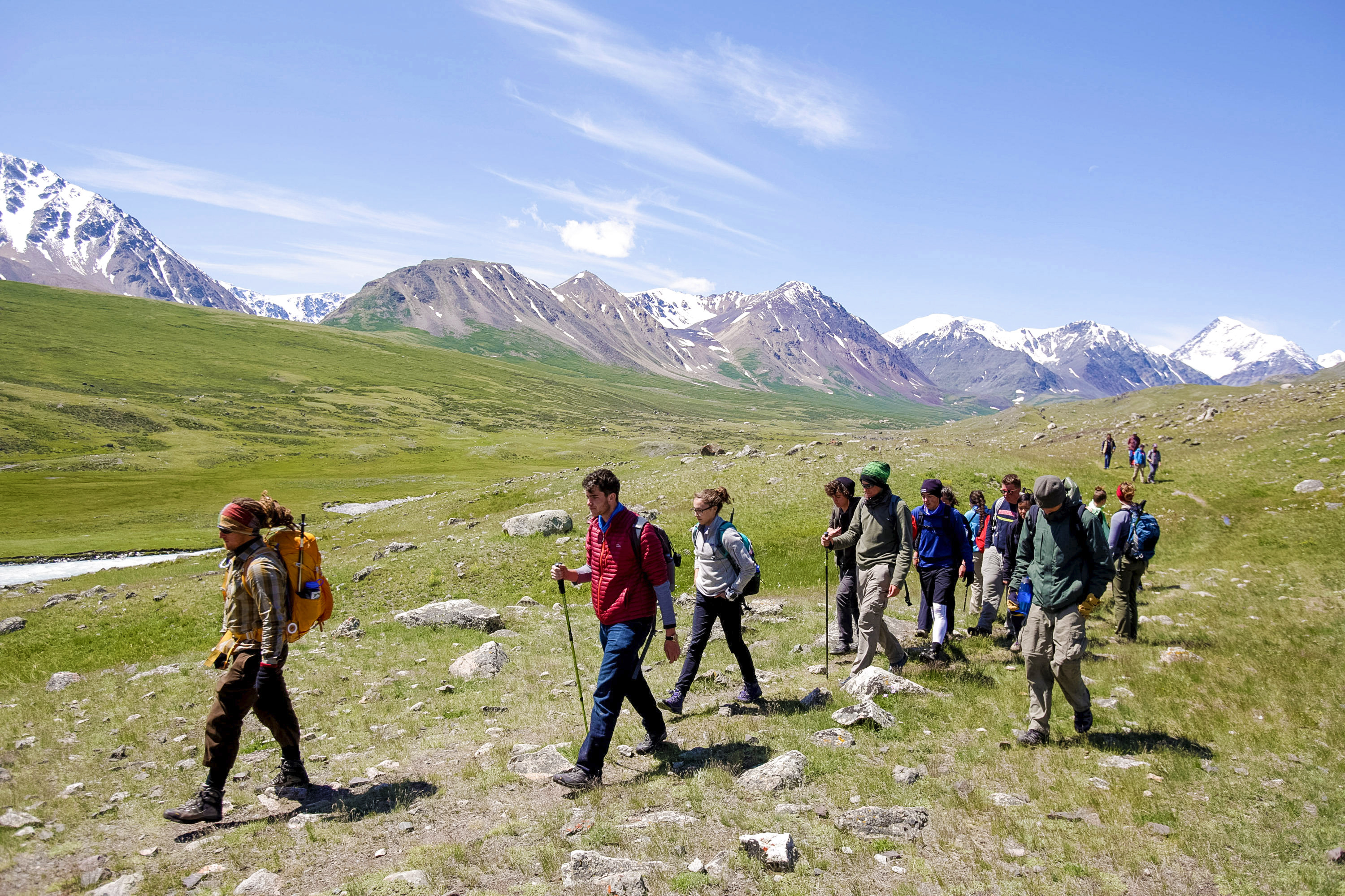 Students hike across a grassy valley with snow-capped mountains behind them