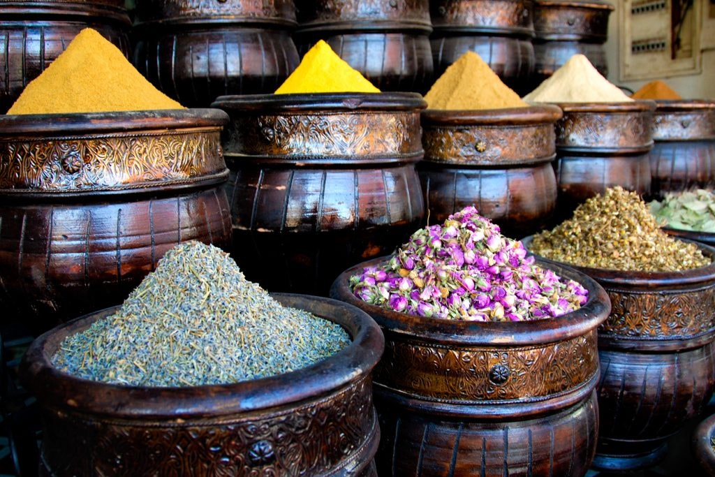 Colorful spices and dried flowers in ornate wooden containers.