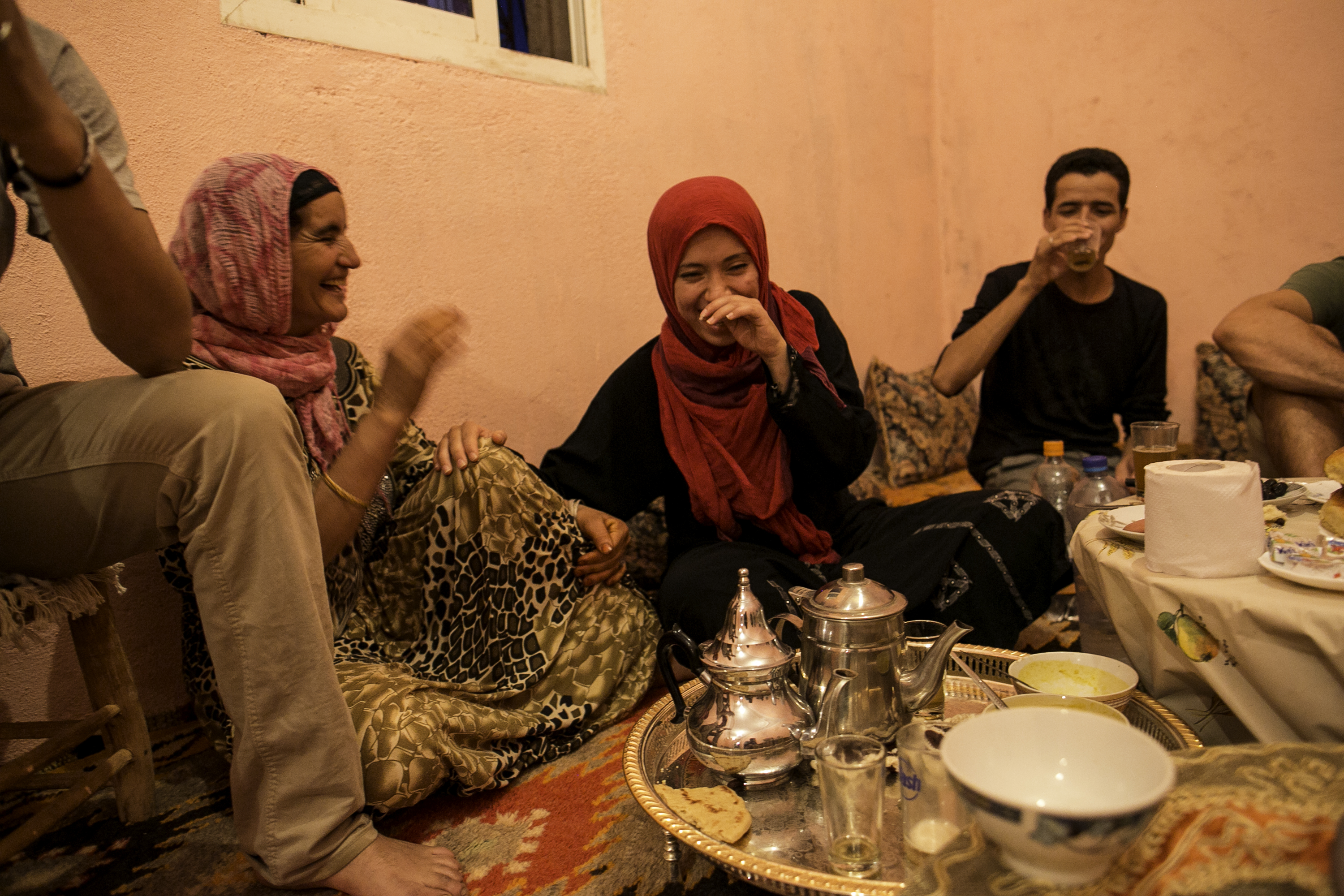 A school trip stop finds students sitting on floor cushions sharing tea and pastries with a host family