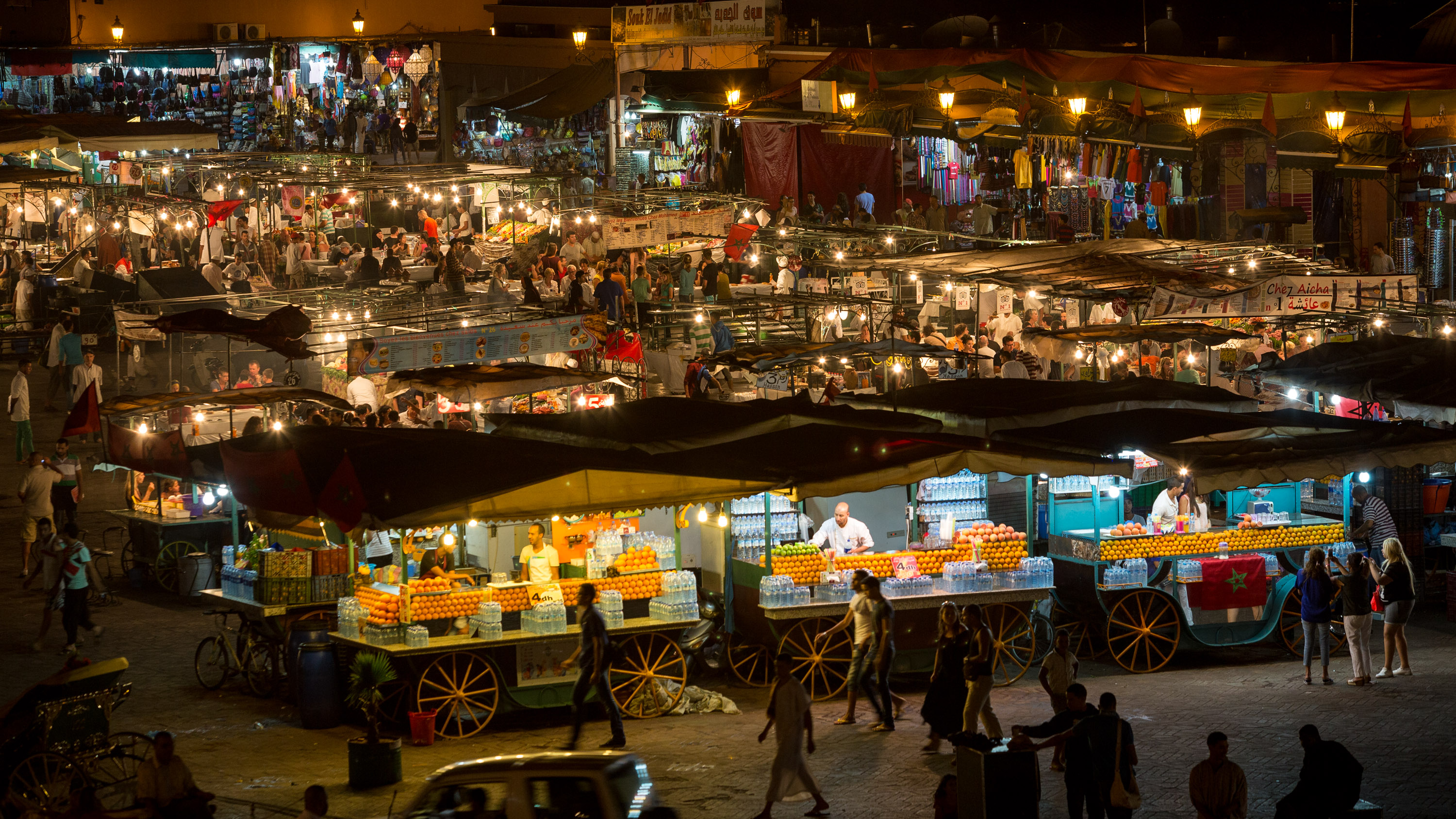 Orange juice carts lit up at night in a bustling Marrakech square