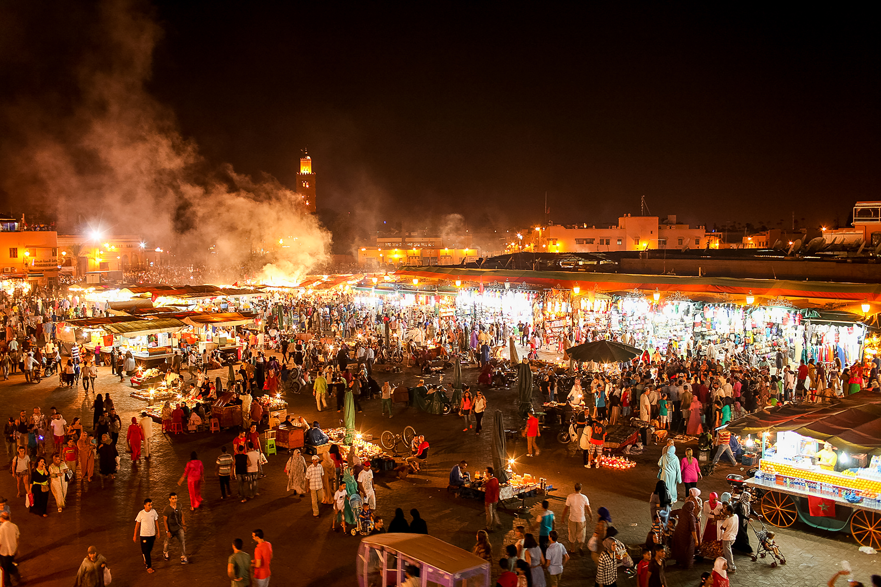 Crowds fill Marrakech's Jemaa el-Fnaa square at night, lit by market stalls and rising smoke