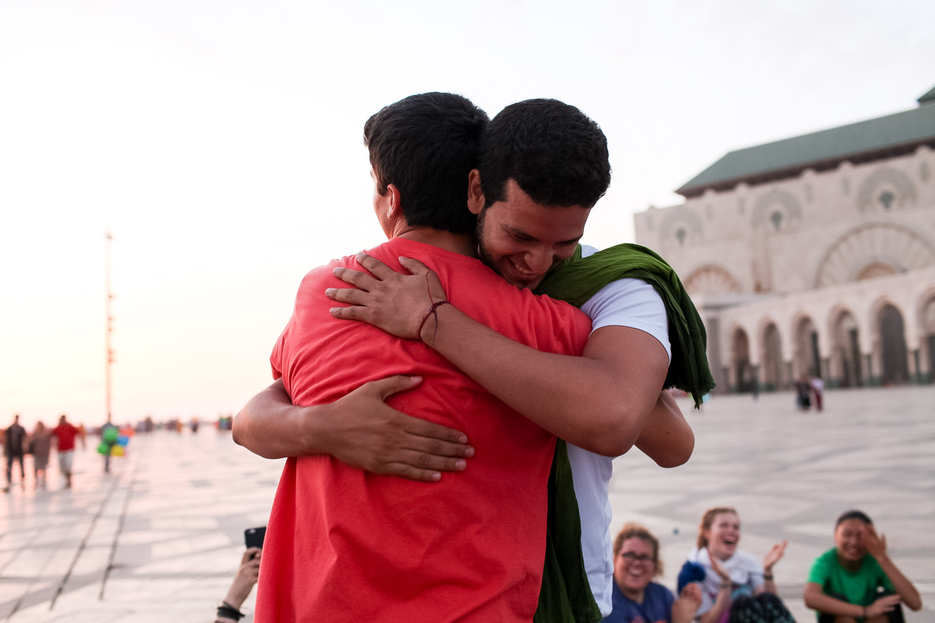 Students embrace in a plaza in front of a large mosque