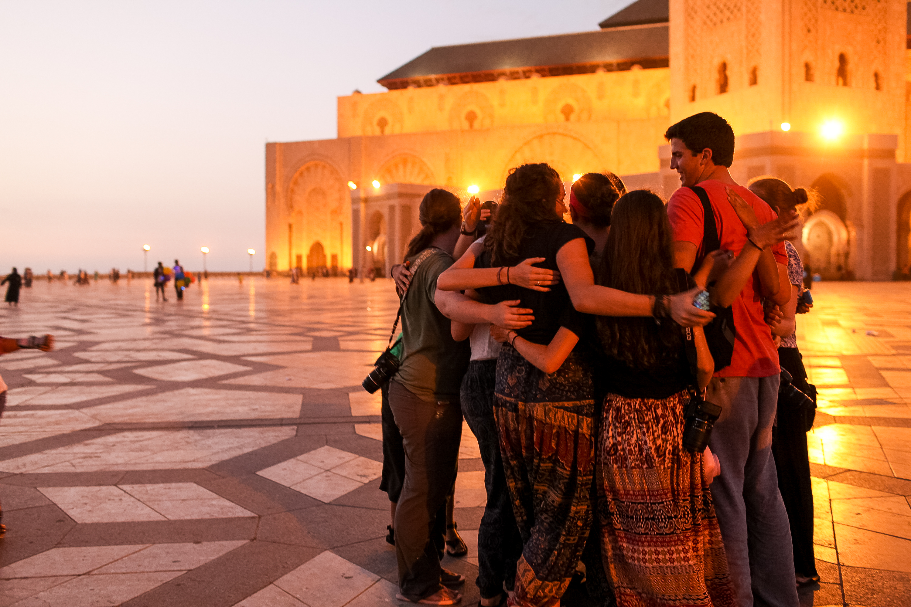 Students embrace in a group hug at dusk in front of the Hassan II Mosque