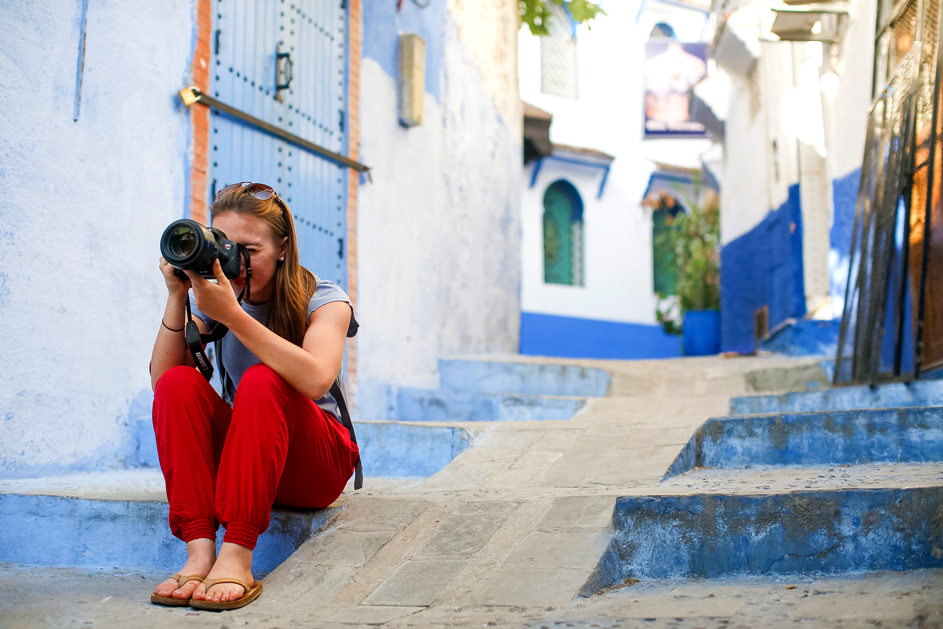 A student sits on steps in the blue-washed medina of Chefchaouen, photographing through a camera lens