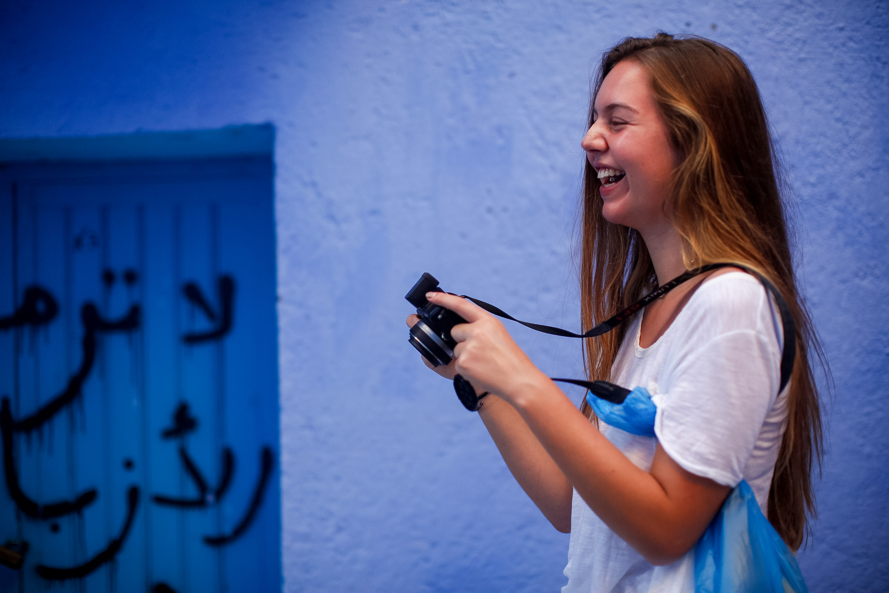 A student laughs while photographing against a blue-painted wall in Chefchaouen