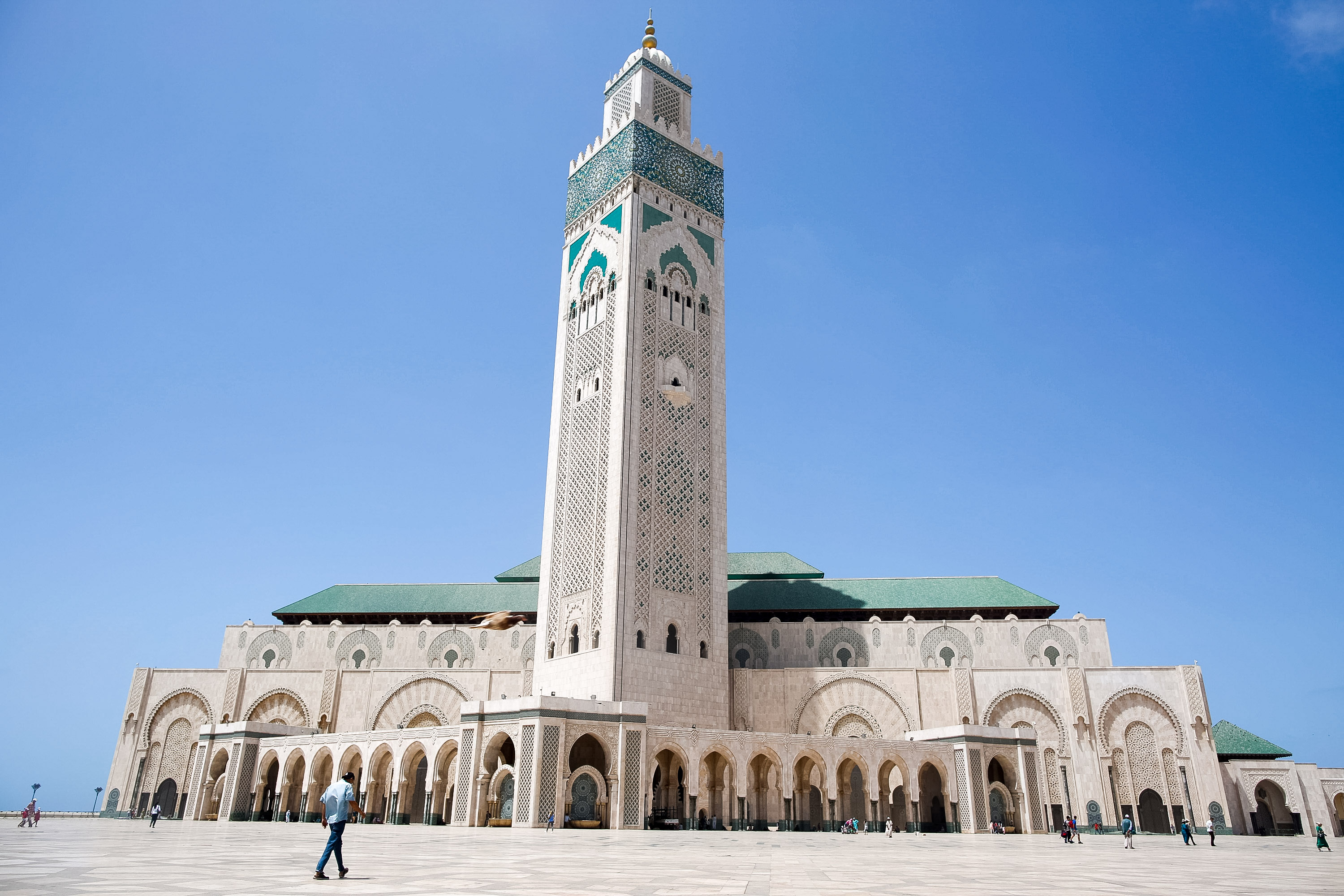 A towering minaret in Morocco rises above a mosque's courtyard under a clear blue sky
