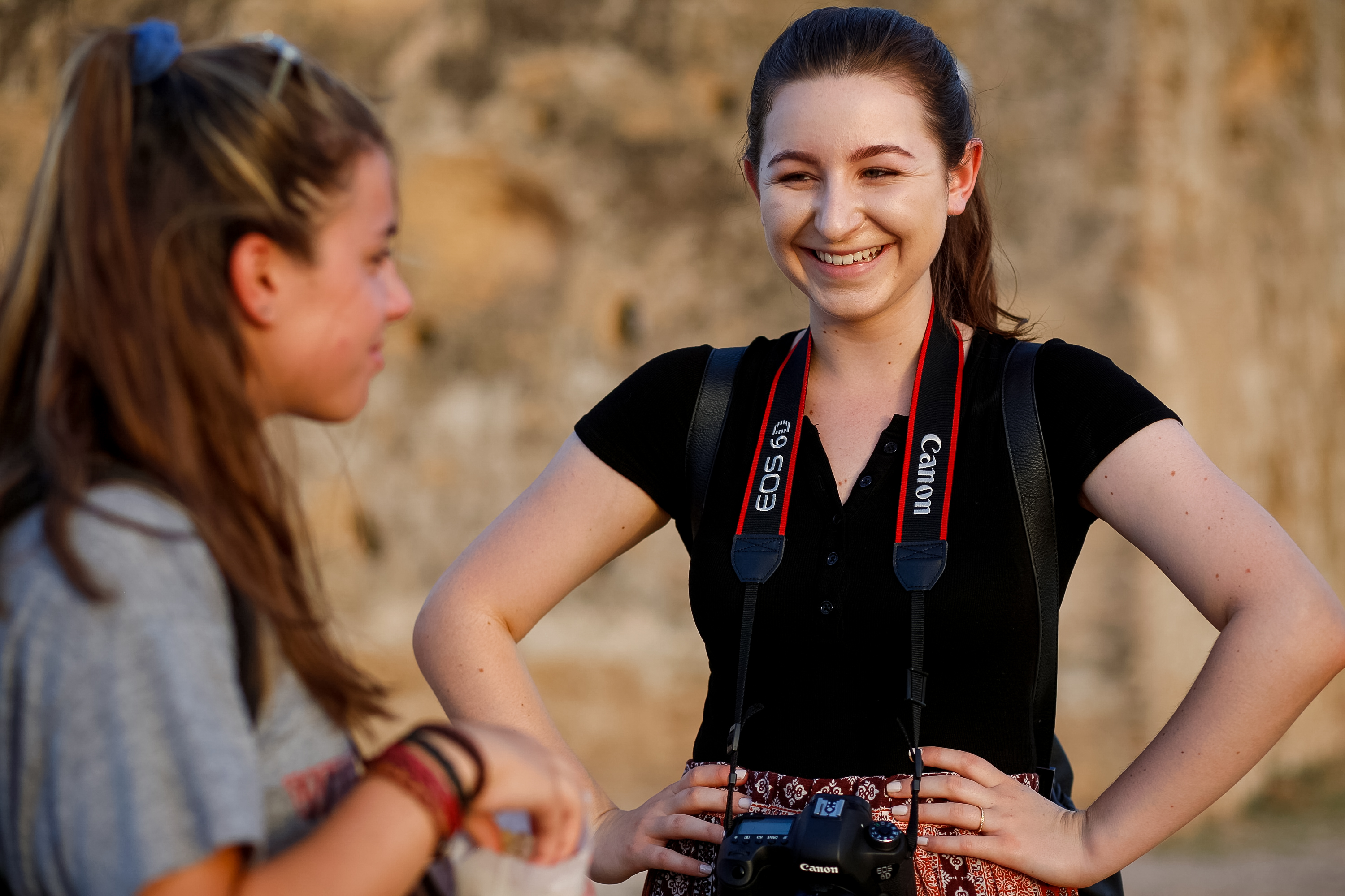 A student with a camera slung around her neck smiles while chatting with another student