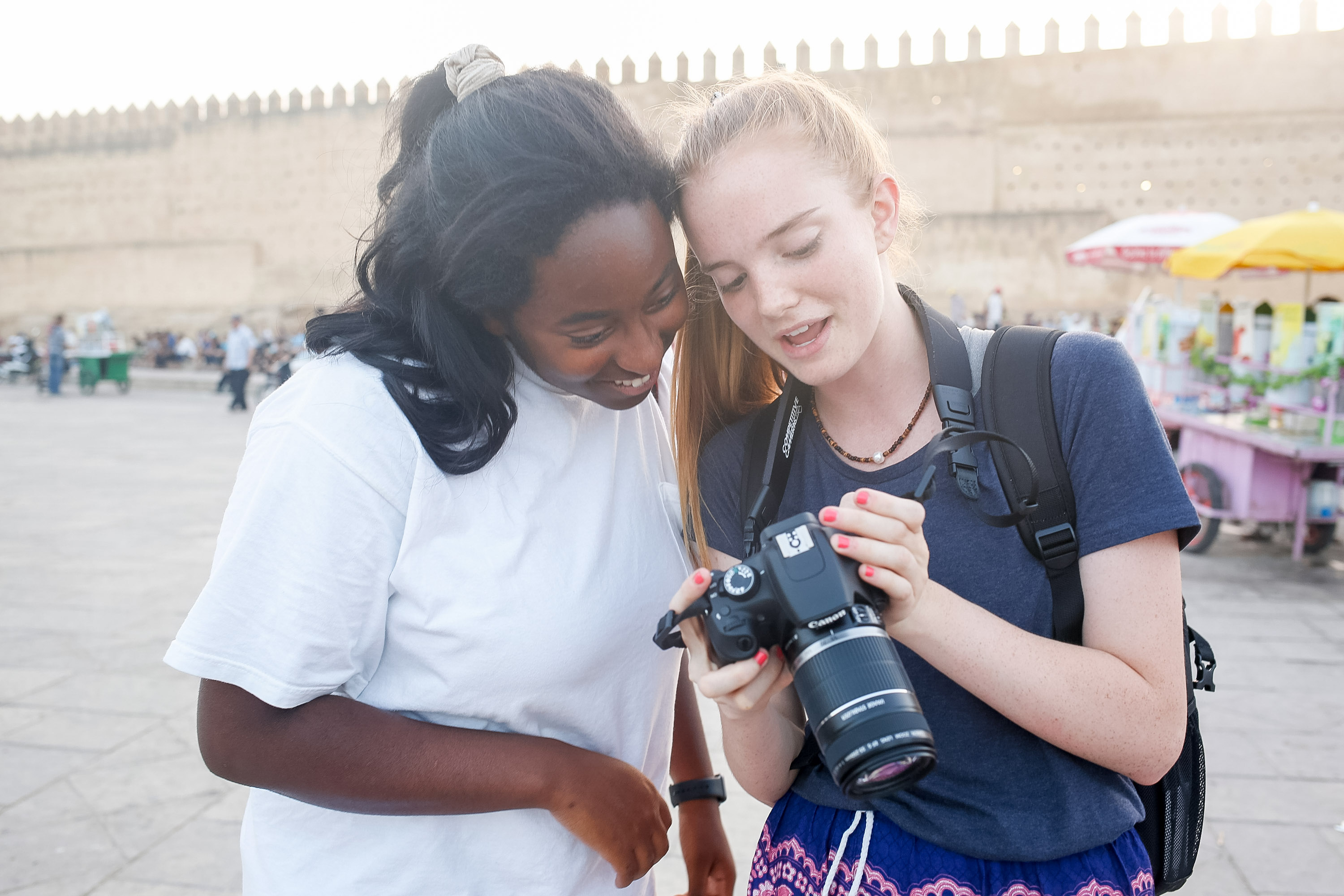 Students in Morocco review photos on a camera screen near an old city wall
