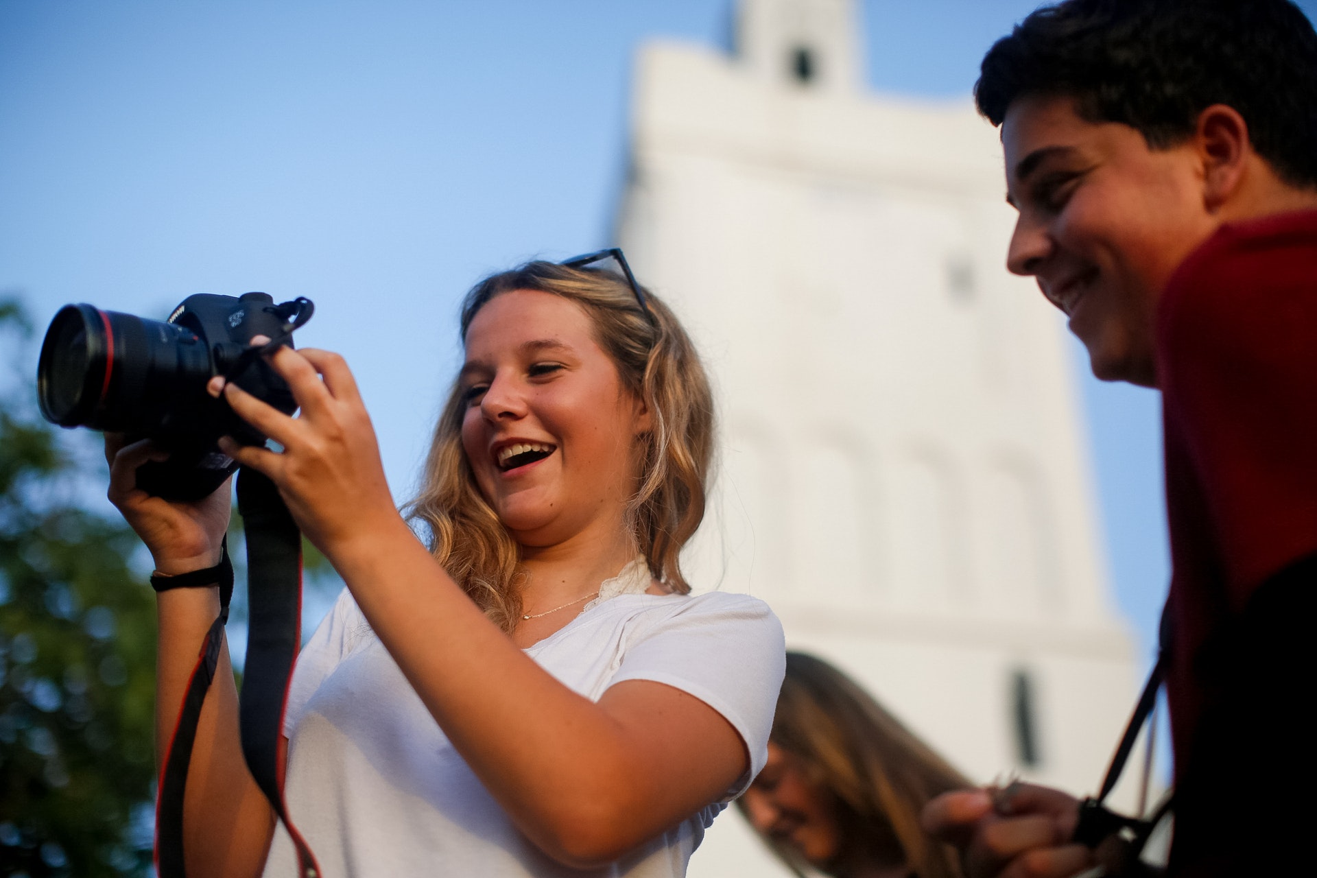 A student in Cuba smiles while taking a photo with a camera near a tower