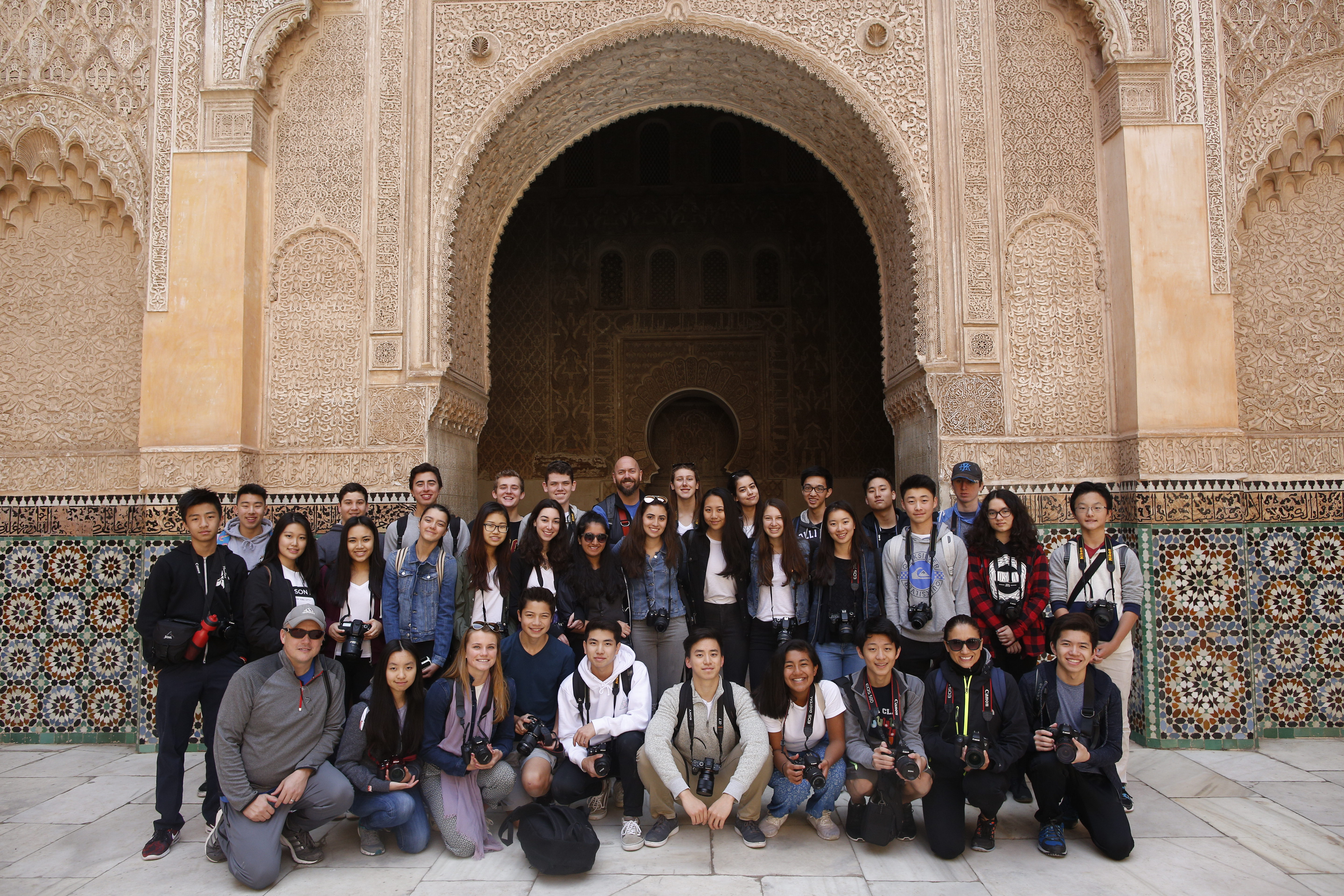 Students pose with cameras beneath an ornately carved archway in Morocco